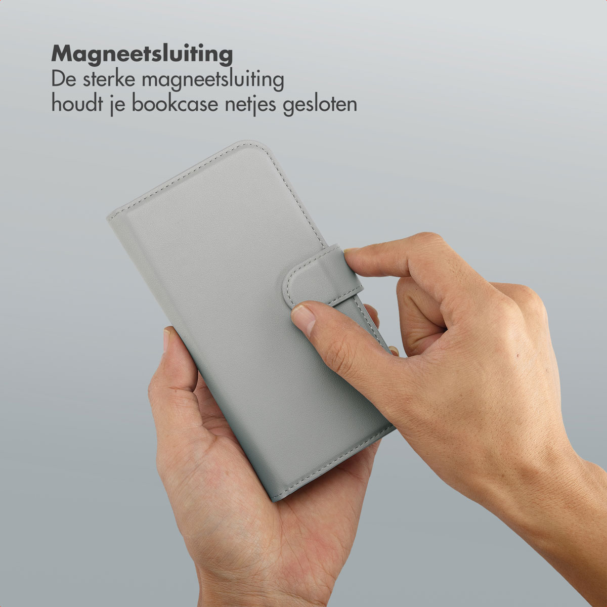 Een hand houdt een grijze telefoonhoes vast. De hand sluit de magnetische sluiting van de hoes. Nederlandse tekst linksboven.