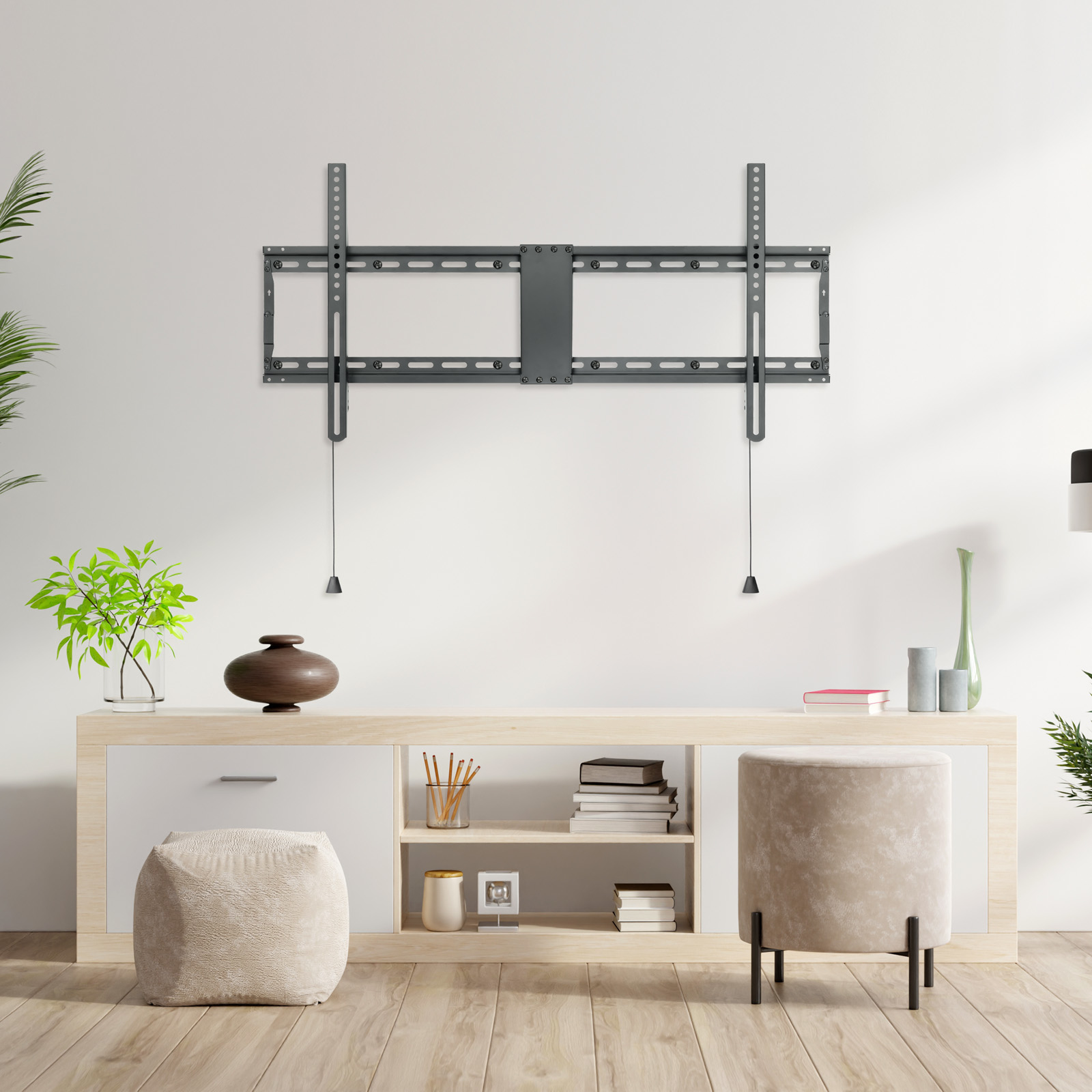 Un soporte de pared para TV está en una pared blanca. Debajo hay un mueble de madera con decoración. Dos otomanas beige están en el suelo.