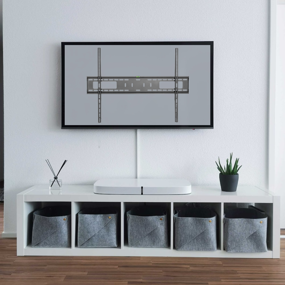 Ein Fernseher mit Halterung an einer weißen Wand. Darunter ein weißes Regal mit Soundbar, Pflanze und grauen Aufbewahrungsboxen. Holzboden.