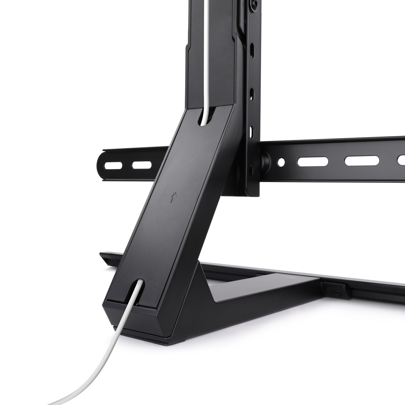 Soporte de TV negro con cable blanco. El soporte tiene una base metálica y una estructura de soporte. El cable pasa por el soporte.