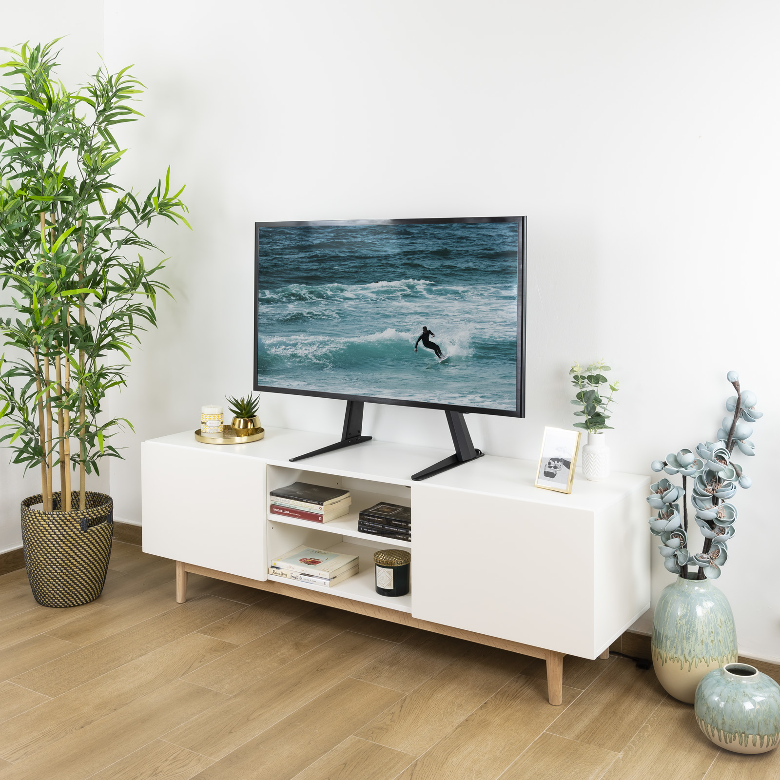 Ein Fernseher zeigt einen Surfer auf einer Welle. Er steht auf einem weißen Schrank mit Dekoration und Pflanzen.