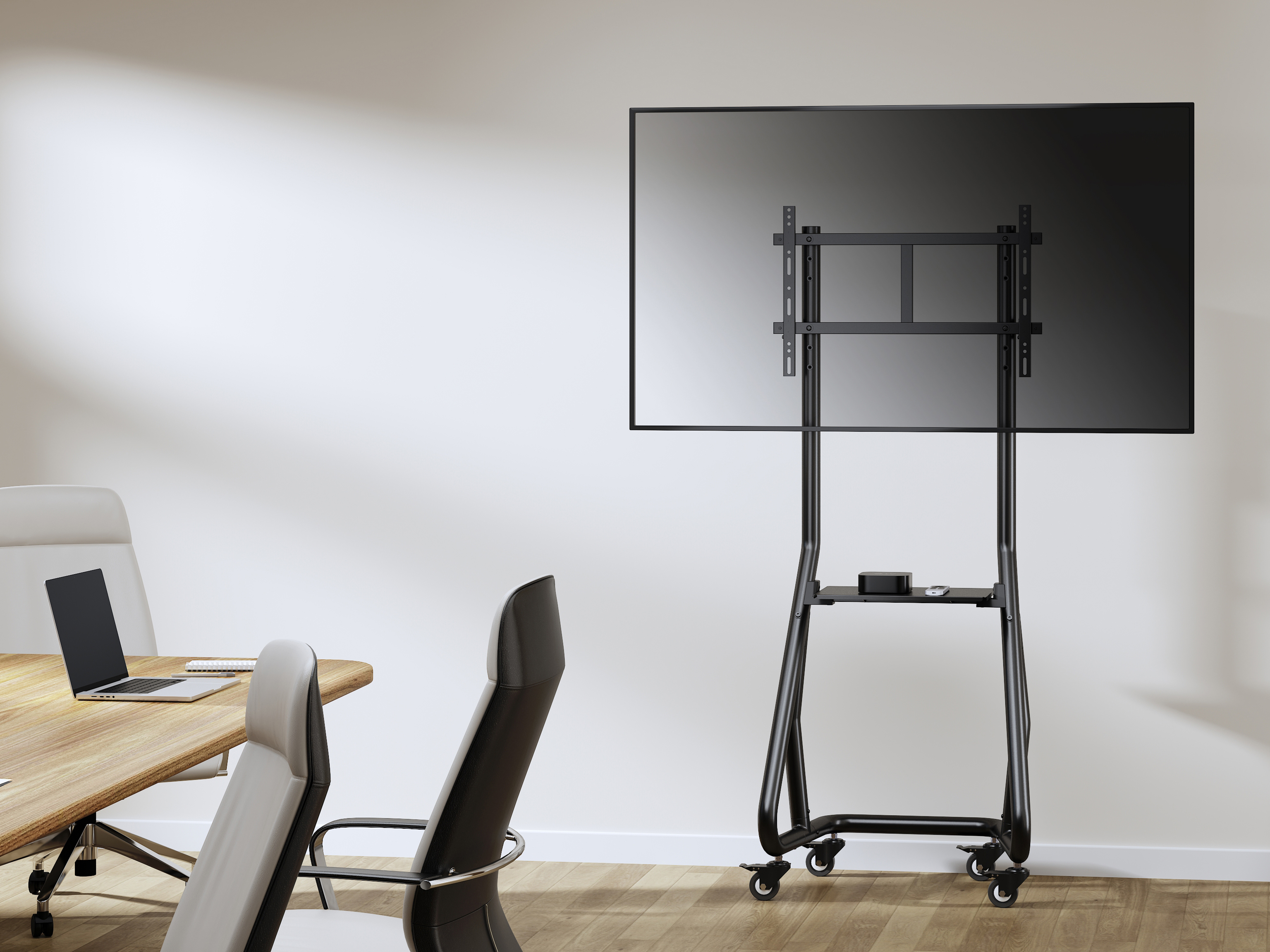 Ein Besprechungsraum mit einem großen Fernseher auf einem Ständer, Tisch, Stühlen und einem Laptop auf dem Tisch, alles vor einer weißen Wand.