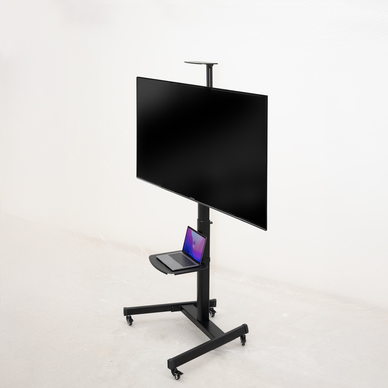 Un televisor negro en un soporte rodante con una computadora portátil en un estante debajo. El fondo es una pared blanca.