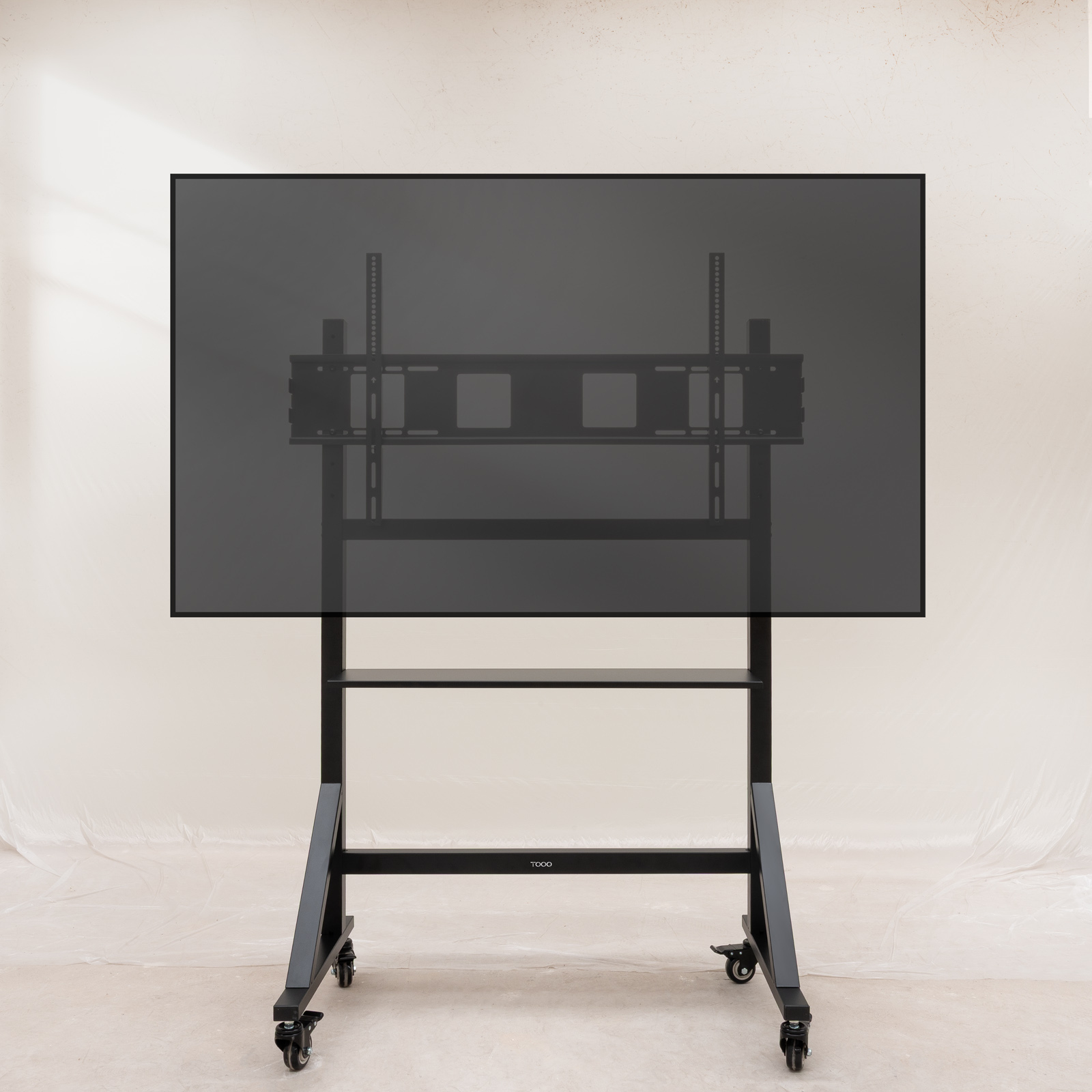 Un televisor negro sobre un soporte rodante. El soporte tiene dos estantes y una marca. El fondo es liso.