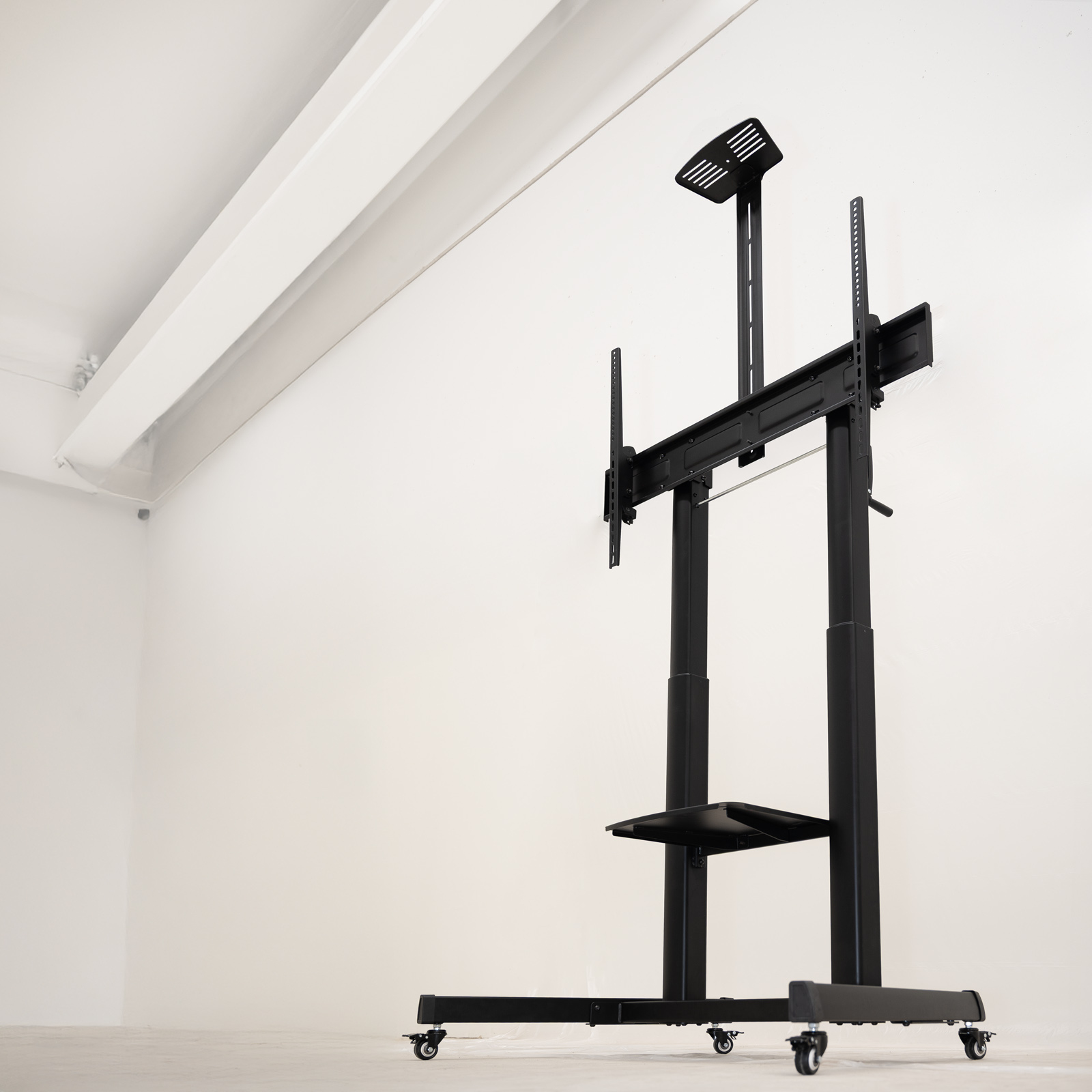 Un soporte de TV negro con ruedas. El fondo es una pared y un techo blancos. El soporte está en el centro.