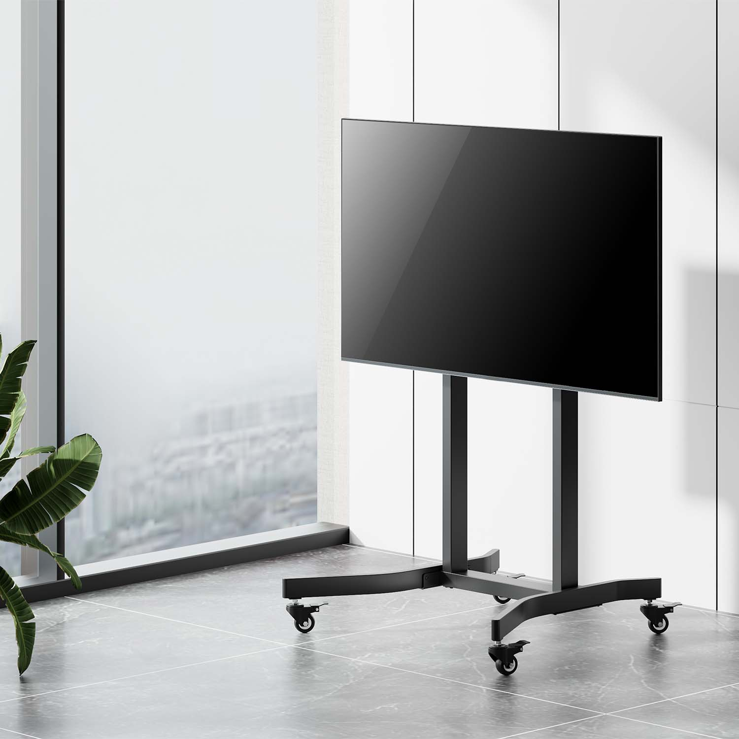 Una grande TV nera su un supporto con ruote si trova di fronte a una finestra che si affaccia su un paesaggio urbano. Una pianta è a sinistra.