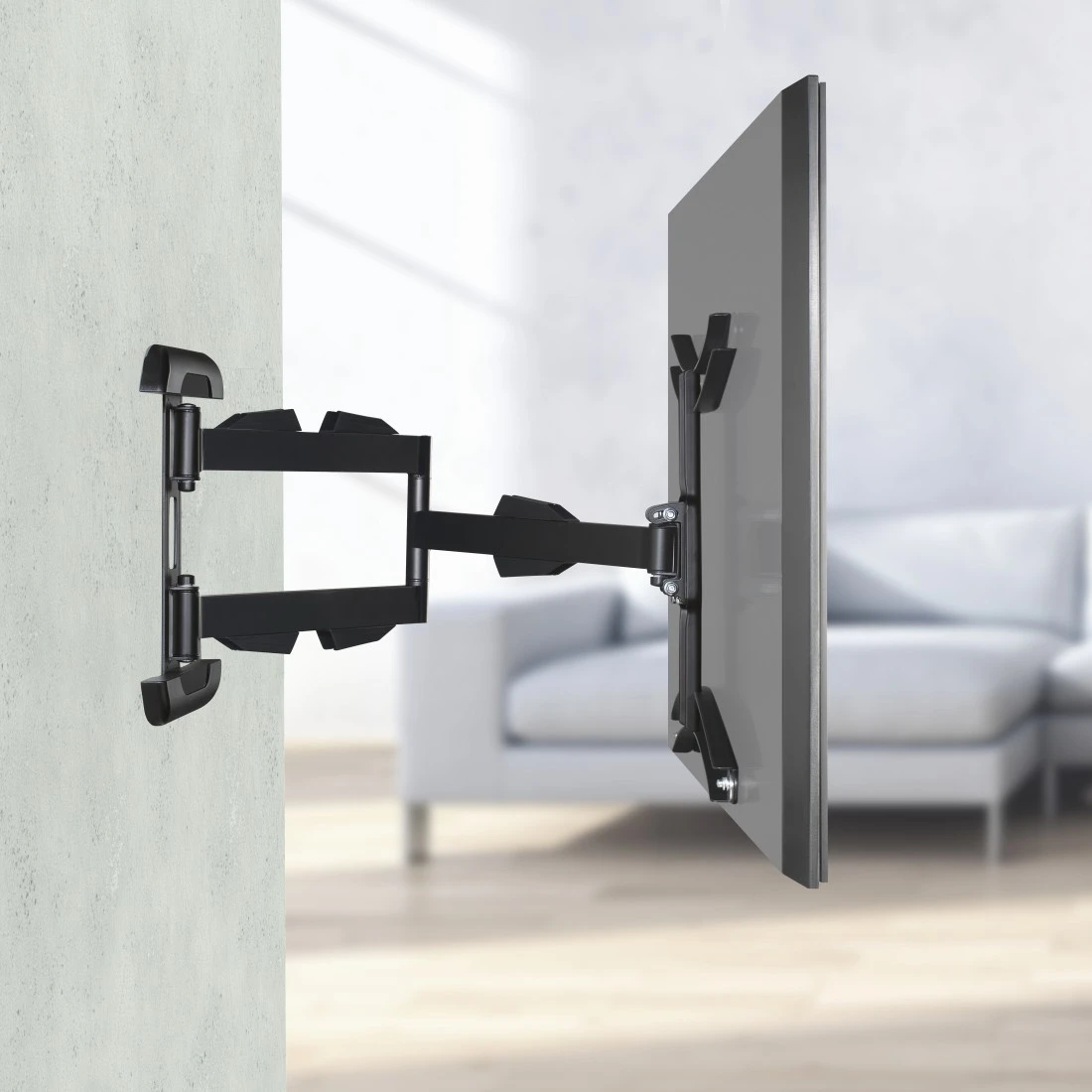 Eine schwarze TV-Wandhalterung ist an einer Wand befestigt. Ein Fernseher ist am Arm montiert. Im Hintergrund ist ein weißes Sofa zu sehen.