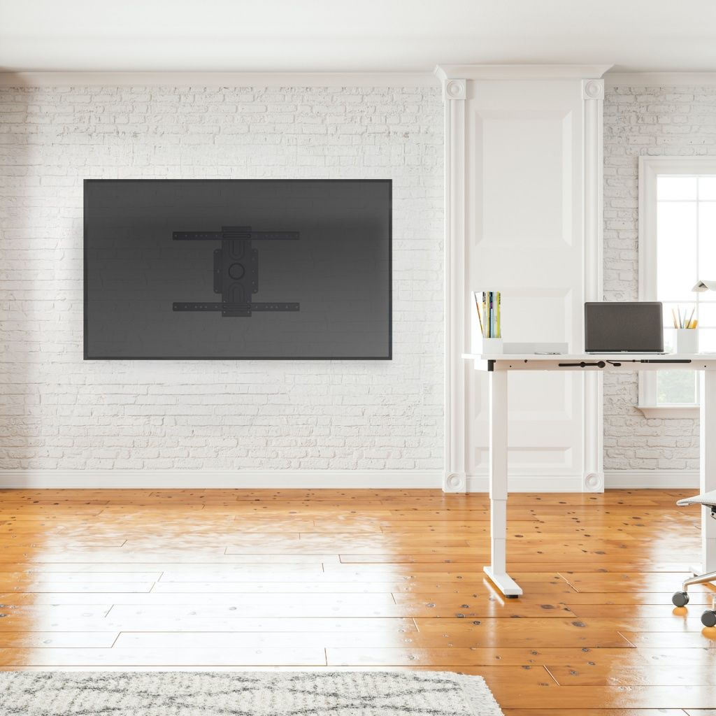 Un moderno ufficio. Una grande TV è montata su un muro di mattoni bianchi. Una scrivania con laptop, libri e matite.