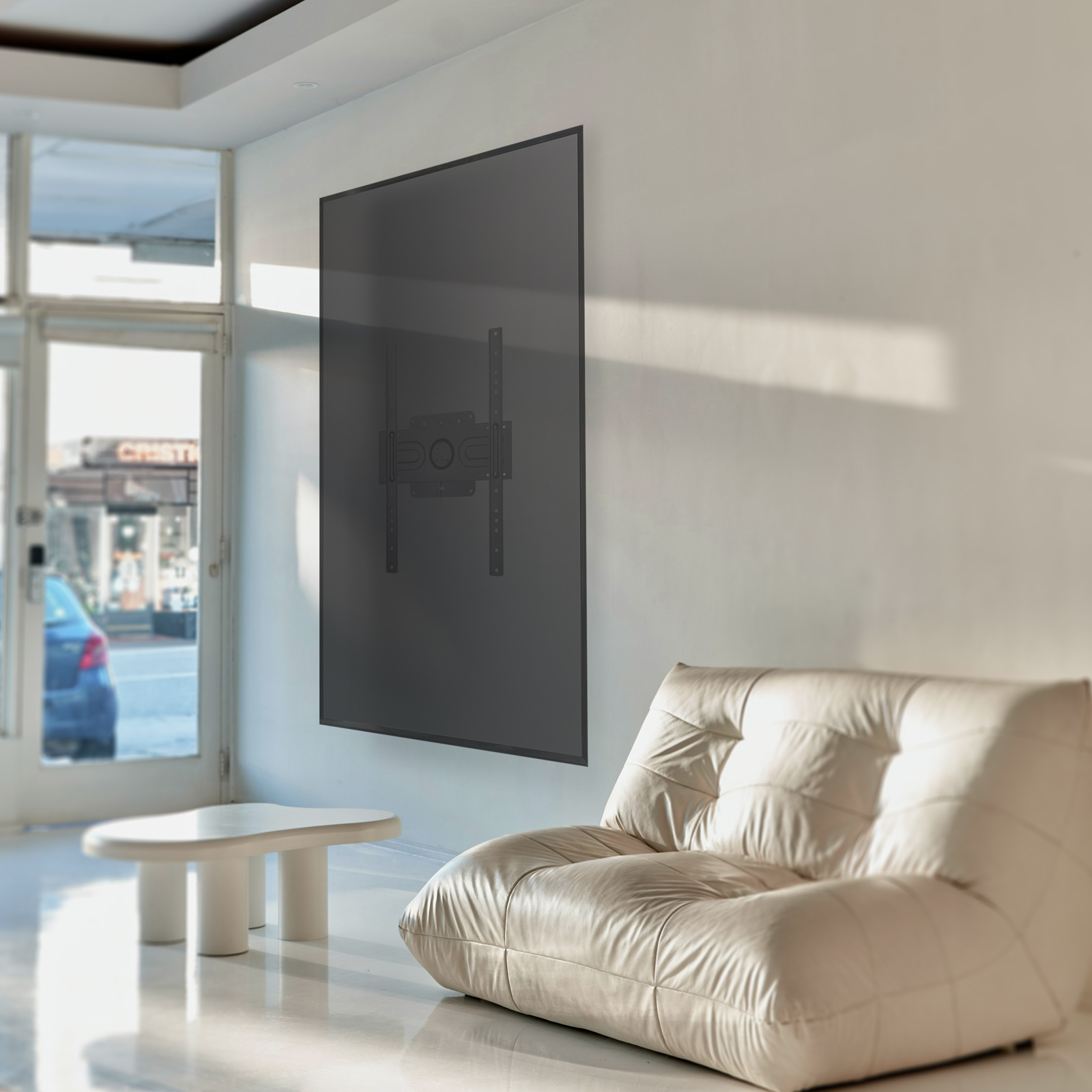 Un supporto TV su un muro bianco, un divano color crema e un tavolo bianco. La luce solare attraversa il muro.
