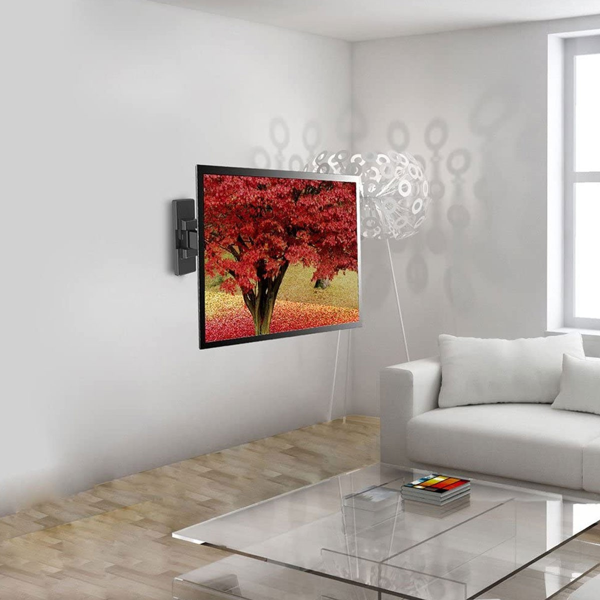 Un televisor muestra un árbol rojo en una pared blanca. Hay un sofá blanco, una mesa de vidrio y una lámpara en la habitación.