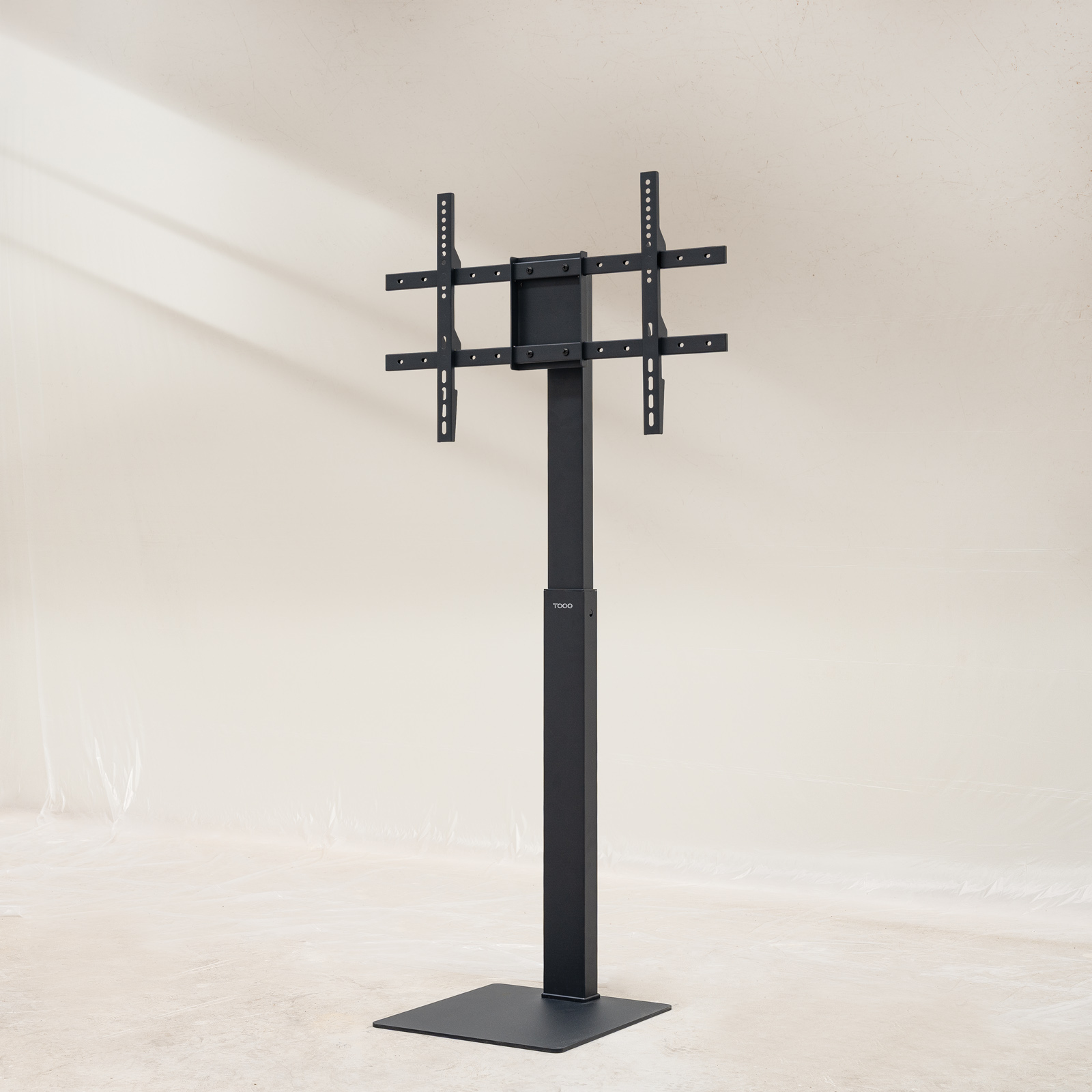 Soporte de TV negro sobre un fondo claro. El soporte tiene una base, un poste vertical y un soporte.