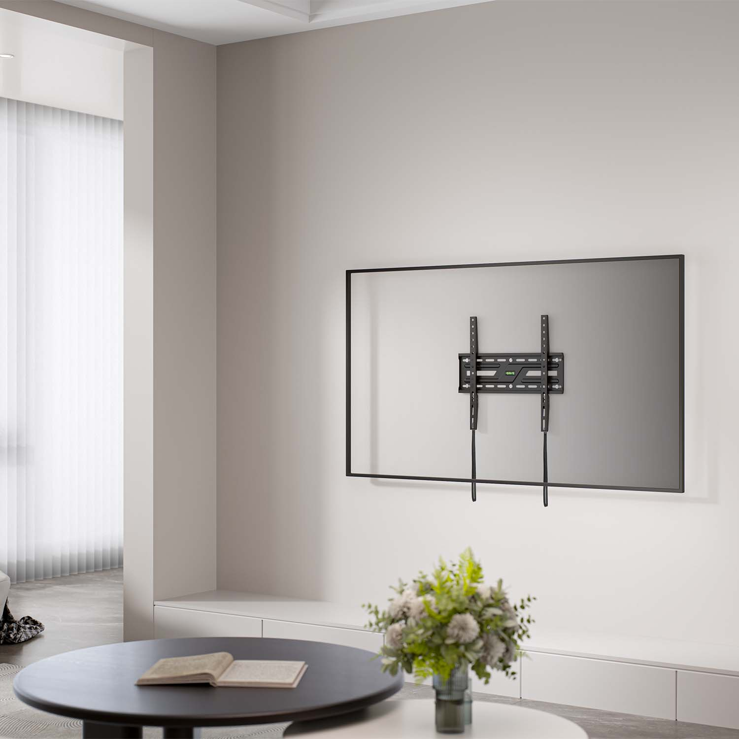 Un soporte de TV montado en la pared sobre una pared blanca. Un ramo de flores y una mesa de centro con un libro delante. Una ventana al fondo.