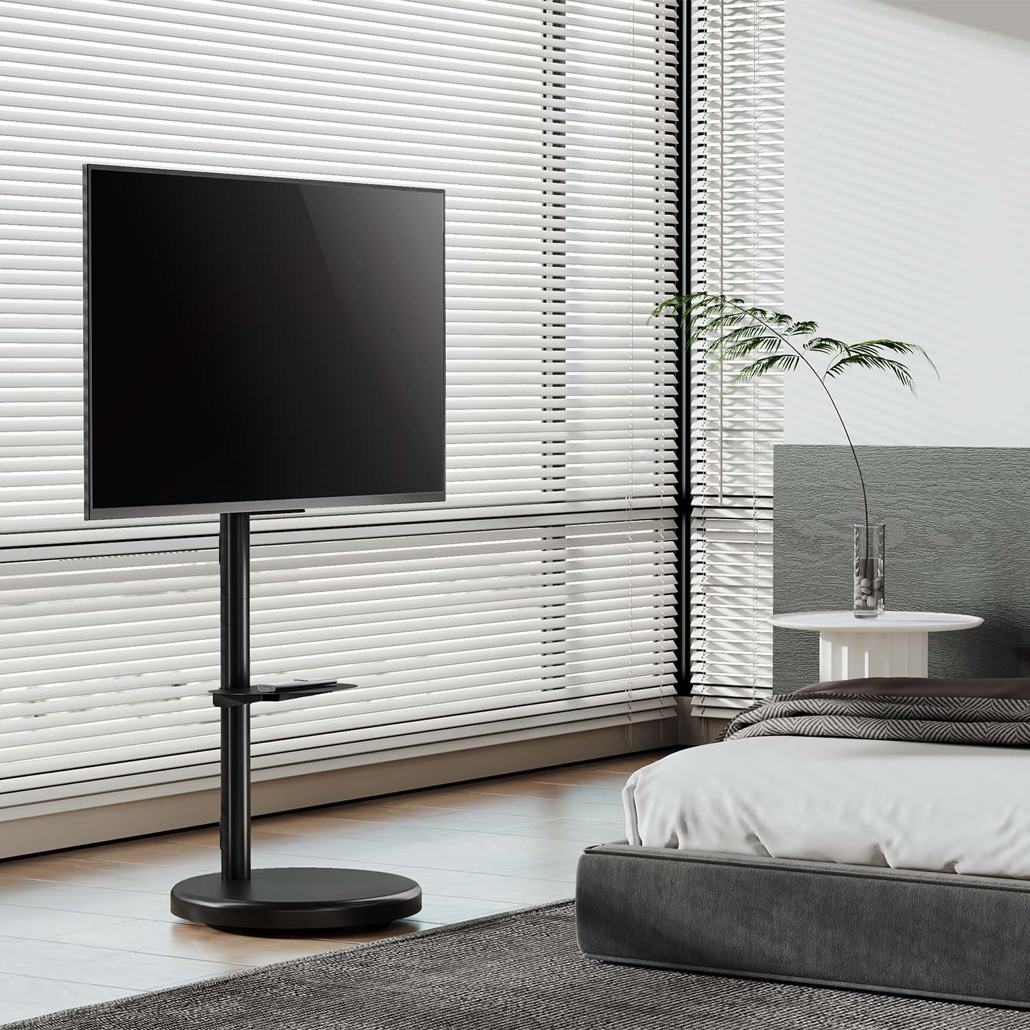 Un televisor negro grande en un soporte en una habitación. Hay persianas detrás del televisor y una cama en la esquina.