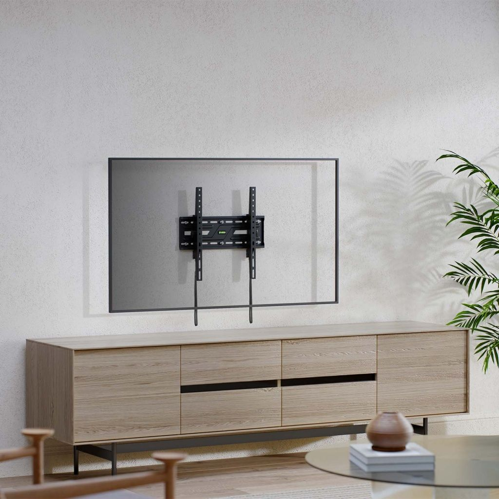Una staffa per TV a parete è su un muro bianco. Sotto c'è un mobile in legno. Una pianta a destra.