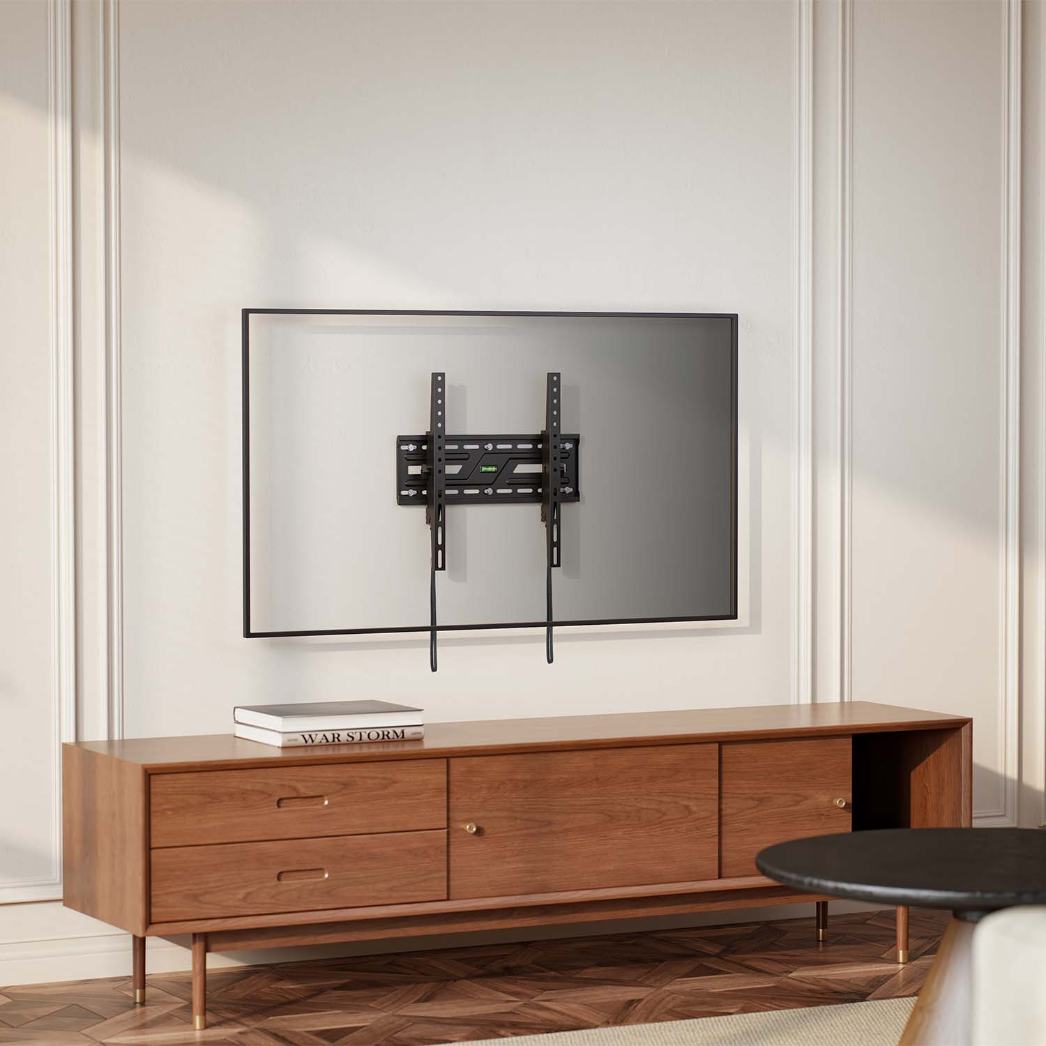 Supporto TV a parete, sopra un mobile in legno. Un libro intitolato 'WAR STORM' è sul mobile. Tavolo nero e tappeto beige nella scena.