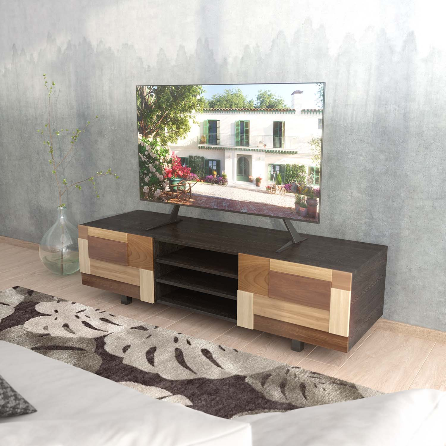 Un televisore su un mobile in legno scuro mostra una scena di casa. Un vaso con rami è a sinistra. Un tappeto e un divano sono in primo piano.