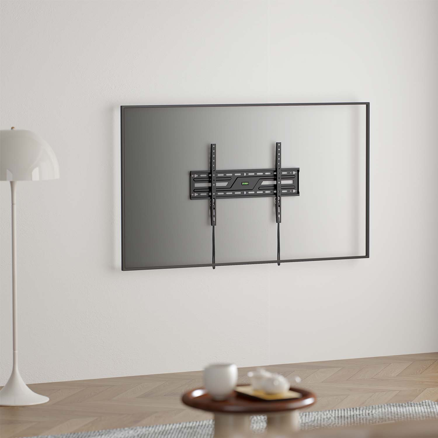 Un televisore è montato su una parete bianca con una cornice nera. Una staffa nera tiene il televisore. Davanti ci sono una lampada e un tavolino.