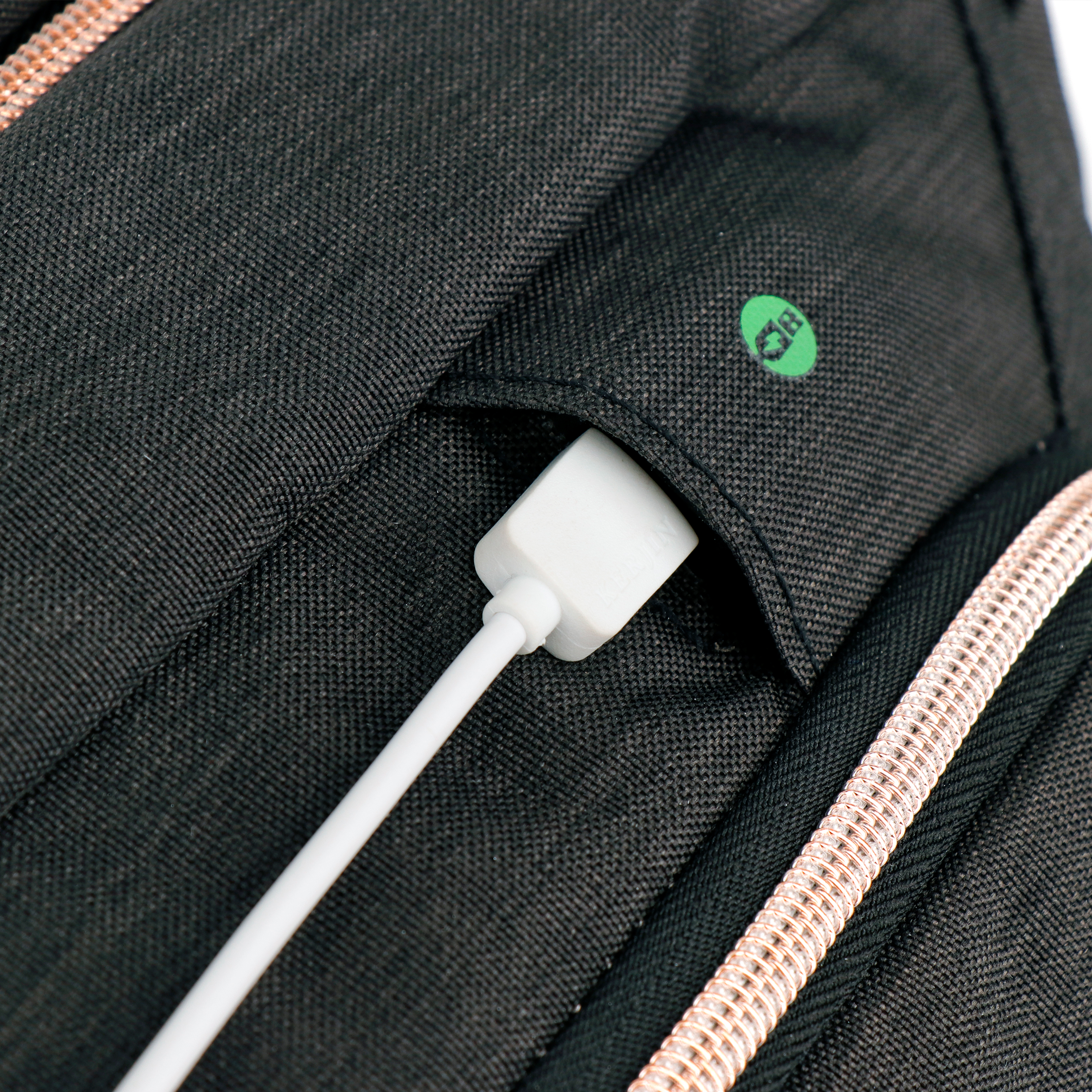 Primo piano di uno zaino nero con un cavo USB bianco collegato. Un logo verde è visibile.
