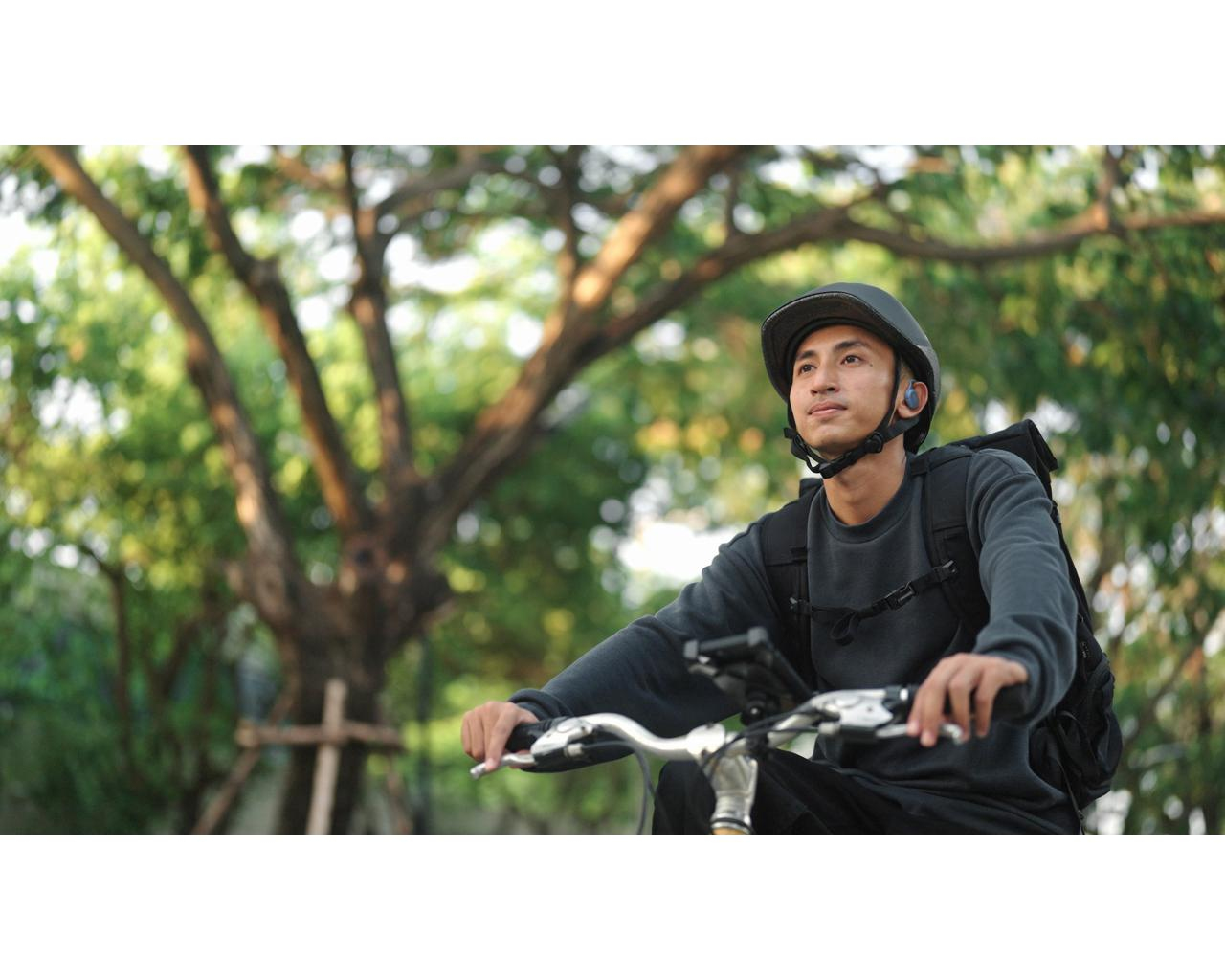 Mężczyzna w kasku jedzie rowerem przez park. Drzewa w tle są rozmyte.