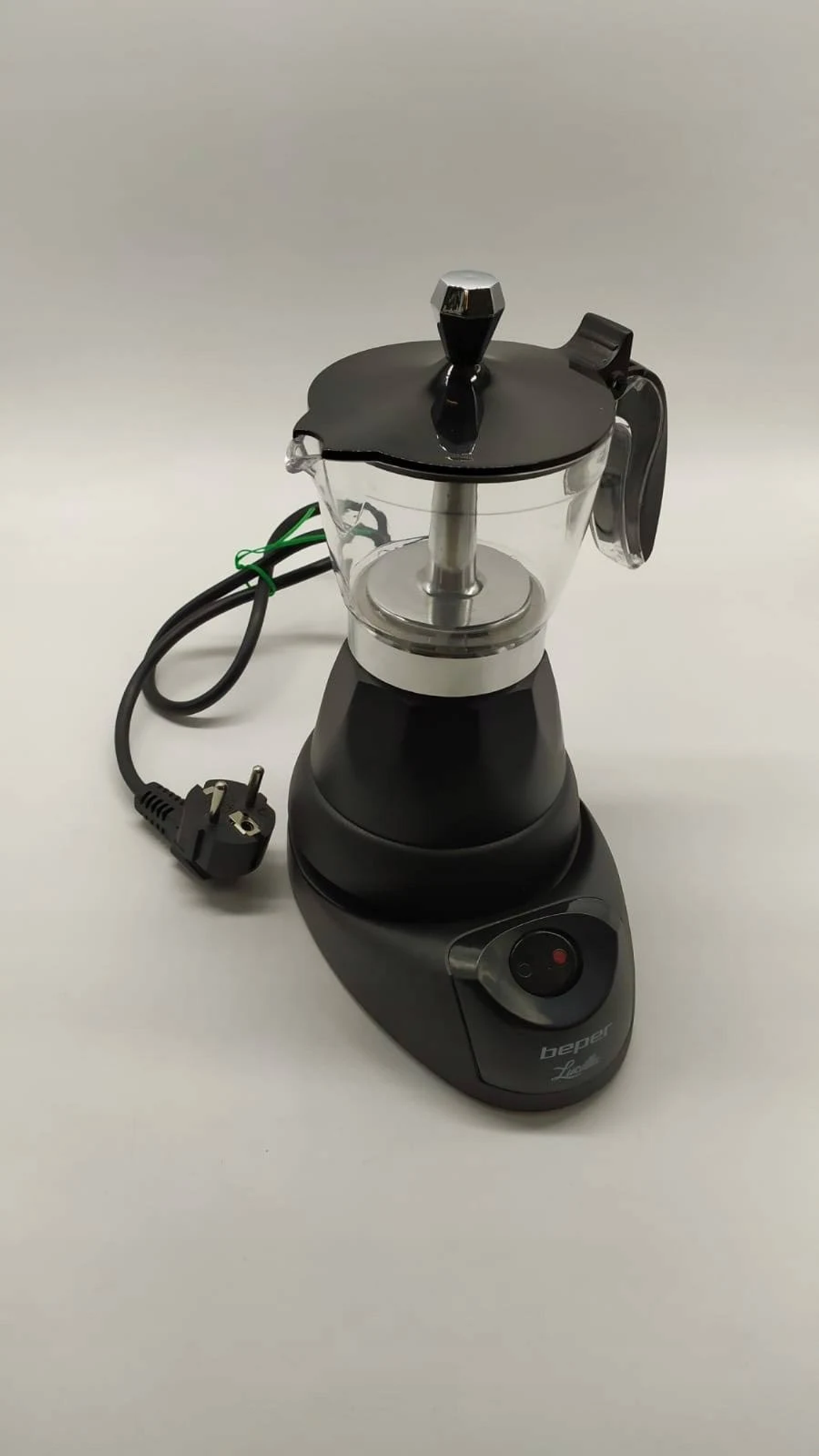 Macchina per caffè elettrica nera su una superficie bianca. Ha un coperchio in vetro, manico e cavo di alimentazione con spina.