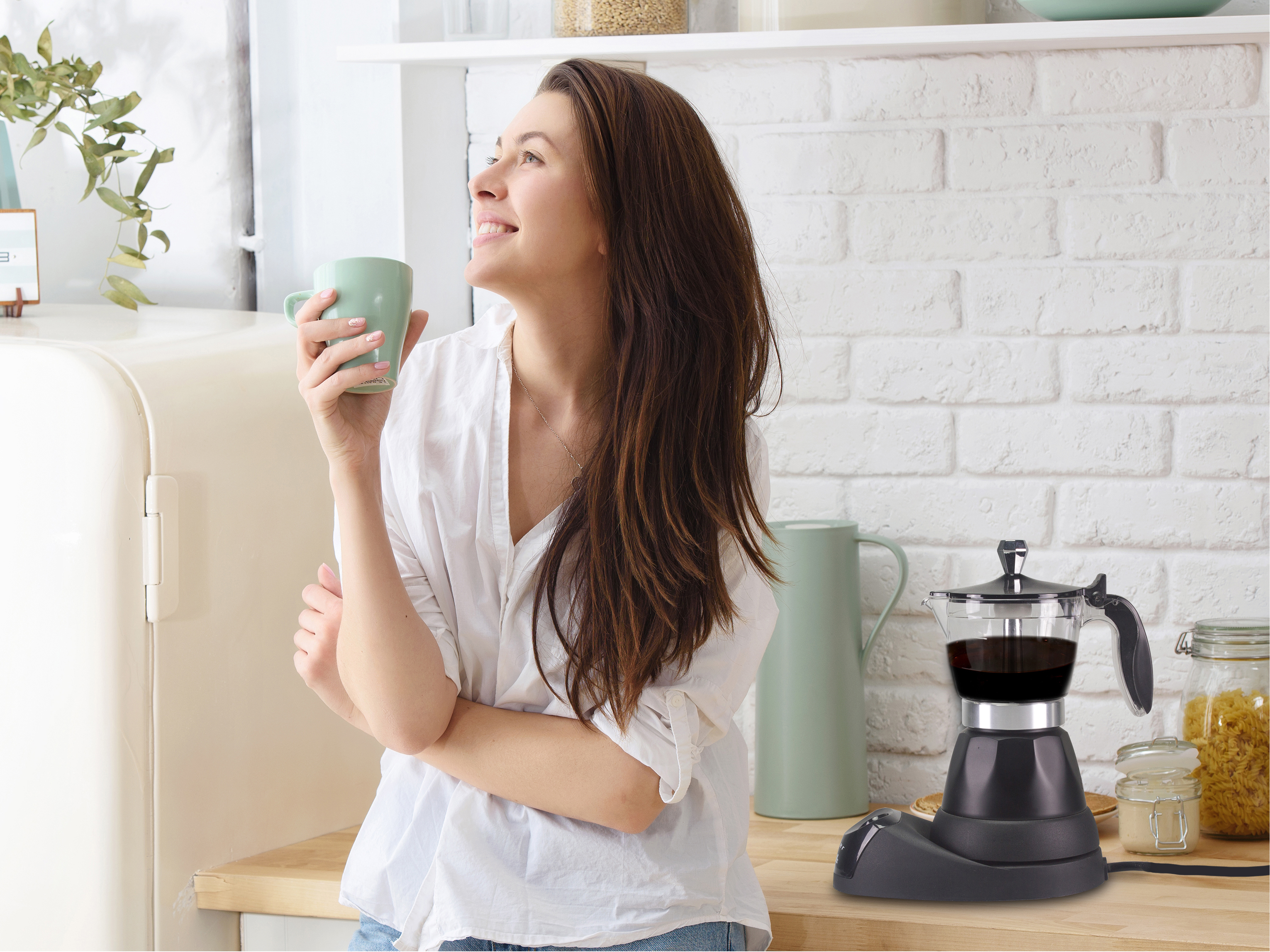 Donna con tazza verde, sorridente, in cucina, con caffettiera.