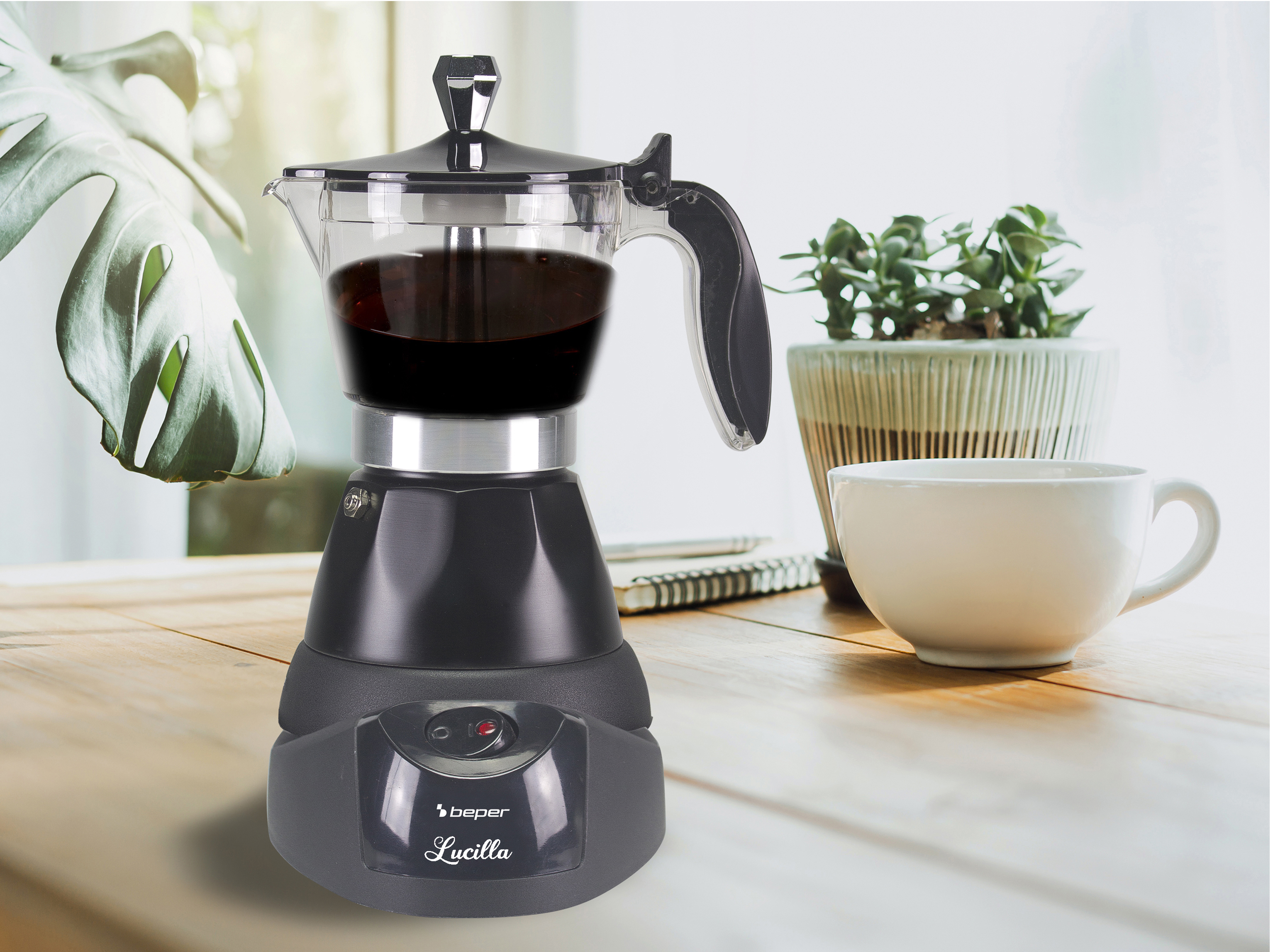 Una caffettiera nera con caffè dentro, una tazza bianca e una pianta su un tavolo di legno.