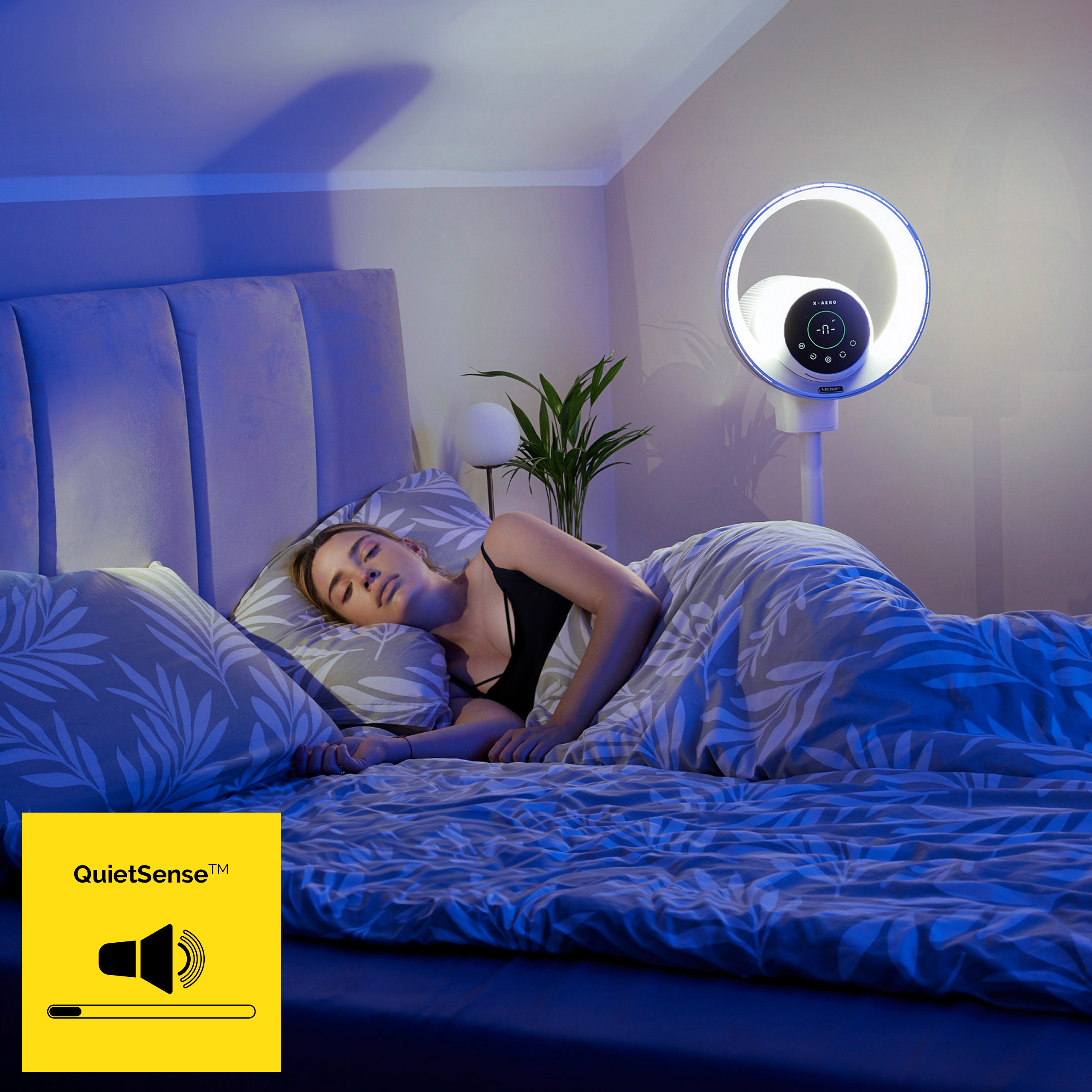 Kobieta śpi w łóżku pod niebieskim światłem. Widoczne jest światło pierścieniowe i logo QuietSense.