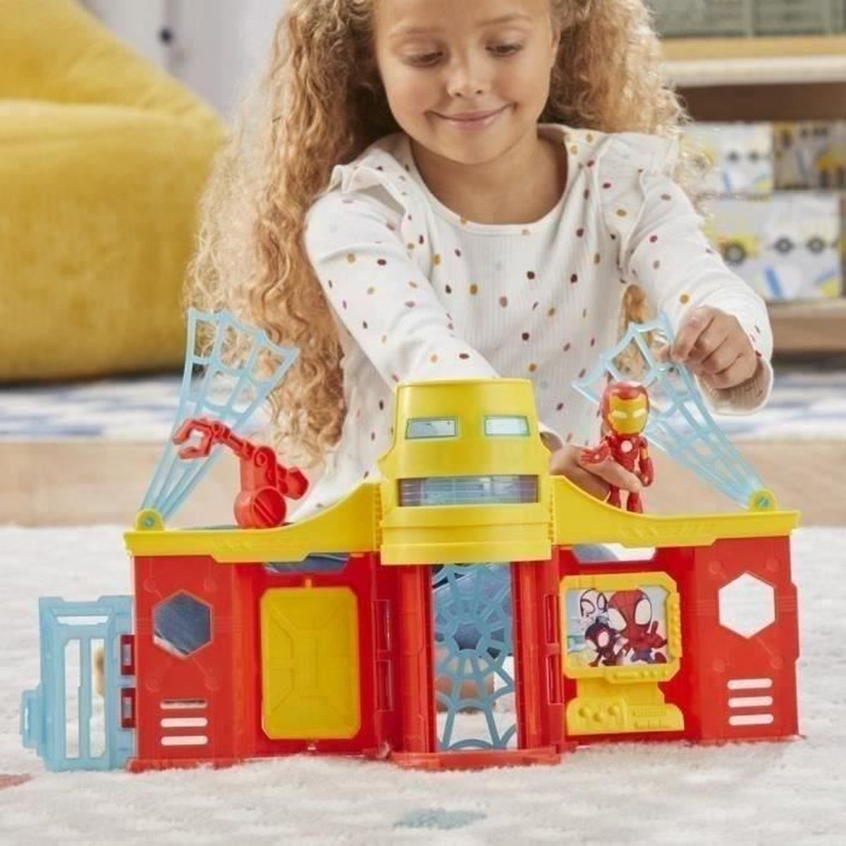 A girl plays with an Iron Man toy set. It features a yellow and red building with an Iron Man figure. The toy has a screen with cartoon characters.