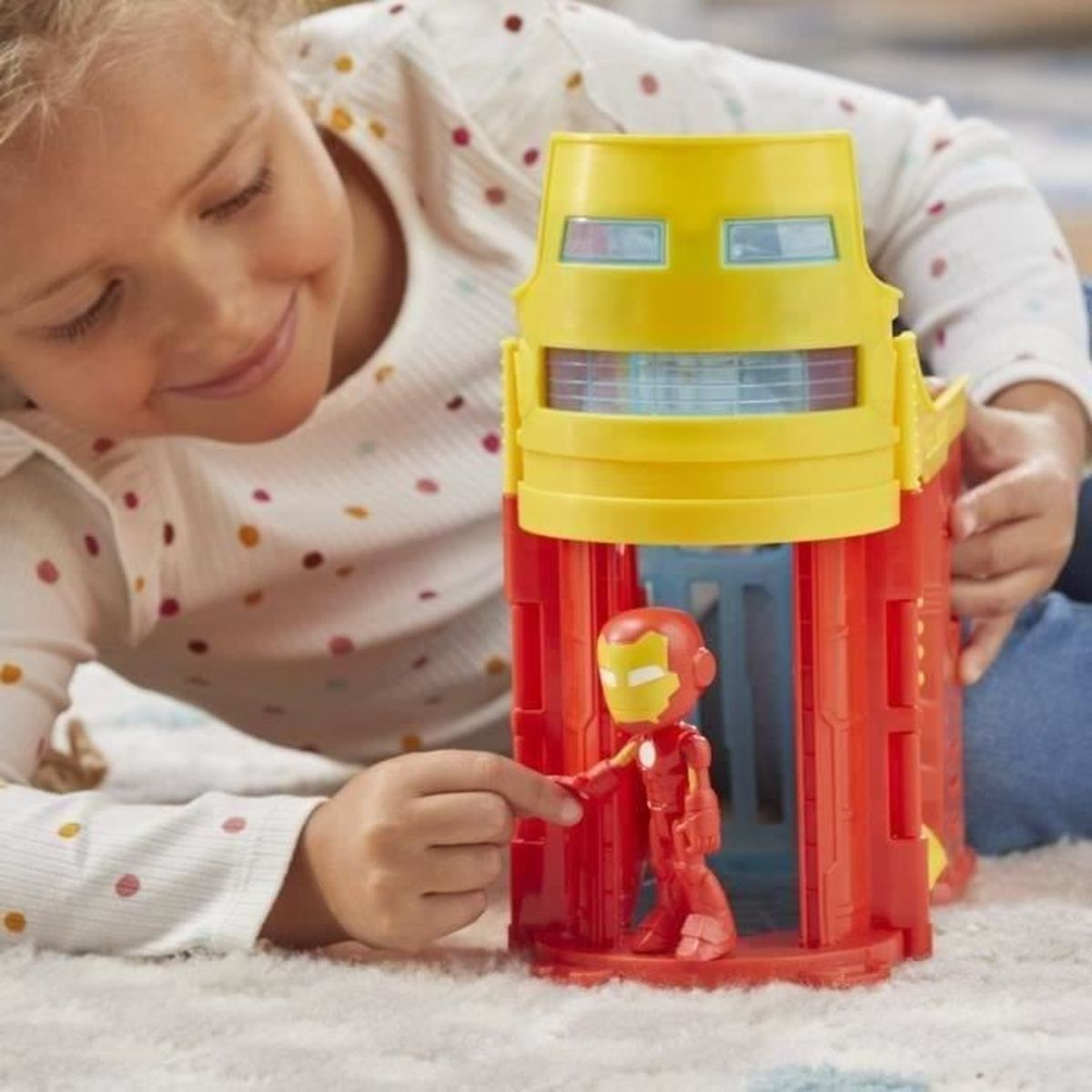 A girl plays with an Iron Man toy. The toy is red and yellow, with an Iron Man figure inside. The girl is smiling.