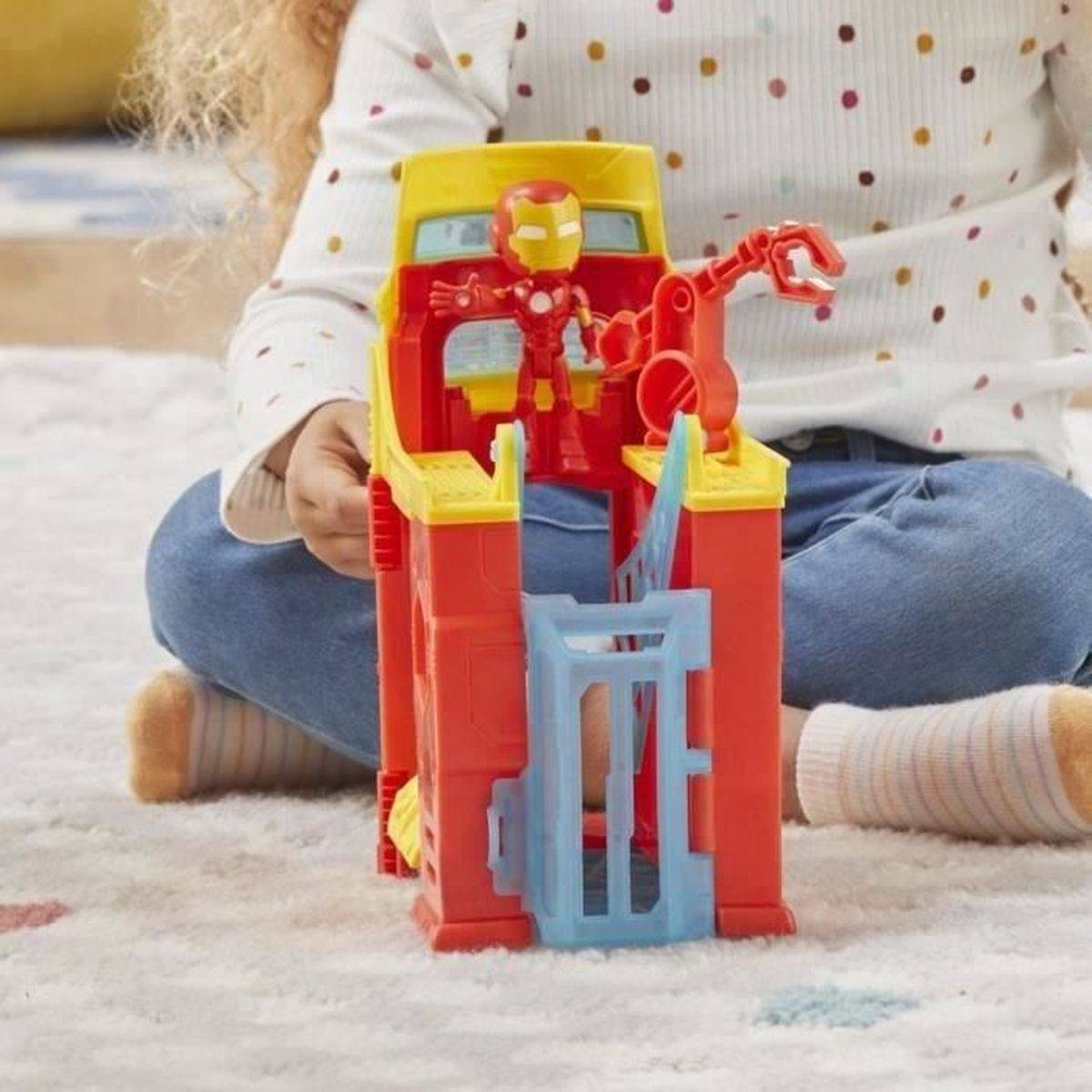 A child plays with an Iron Man toy set. The set is red and yellow. The child is wearing a white shirt and blue jeans.