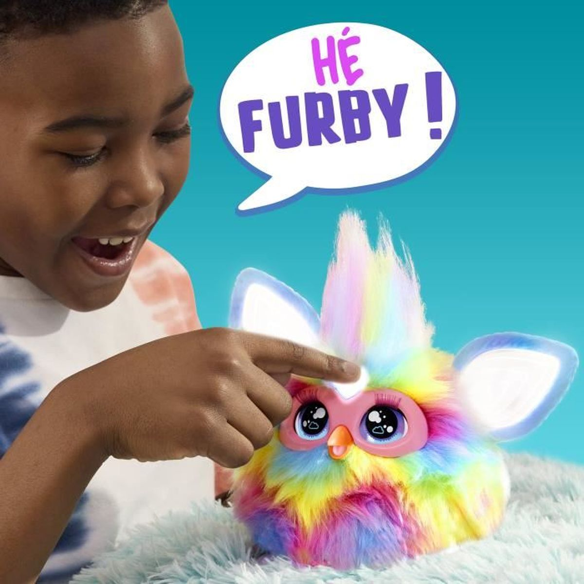 Uśmiechnięty chłopiec wskazuje na kolorową zabawkę Furby. Furby ma świecące uszy i dymek z napisem 'HÉ FURBY!'