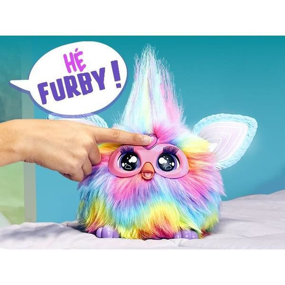 Kolorowa zabawka Furby z ręką dotykającą jej głowy. Furby ma duże oczy i dymek z napisem 'HE FURBY!'