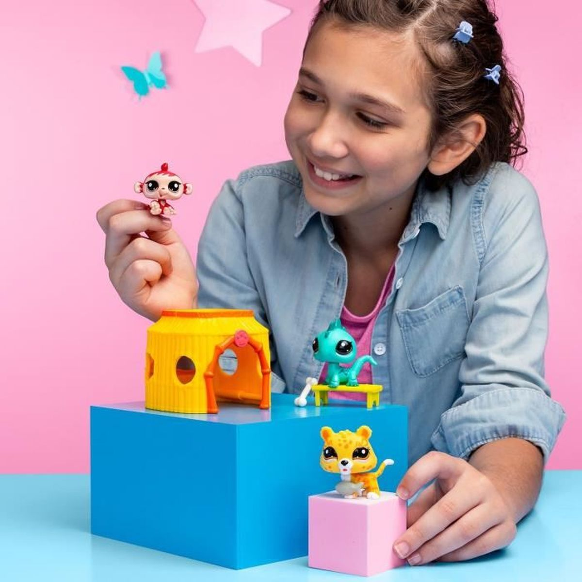 Una niña sonríe, sosteniendo un juguete de mono. Otros juguetes incluyen una casa, un guepardo y un lagarto. Una mariposa y una estrella están en el fondo.