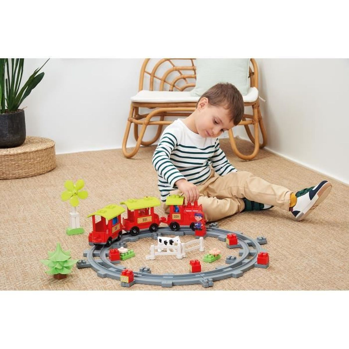Un bambino gioca con un set di trenini giocattolo su un tappeto. Il set include un treno rosso, binari e accessori.
