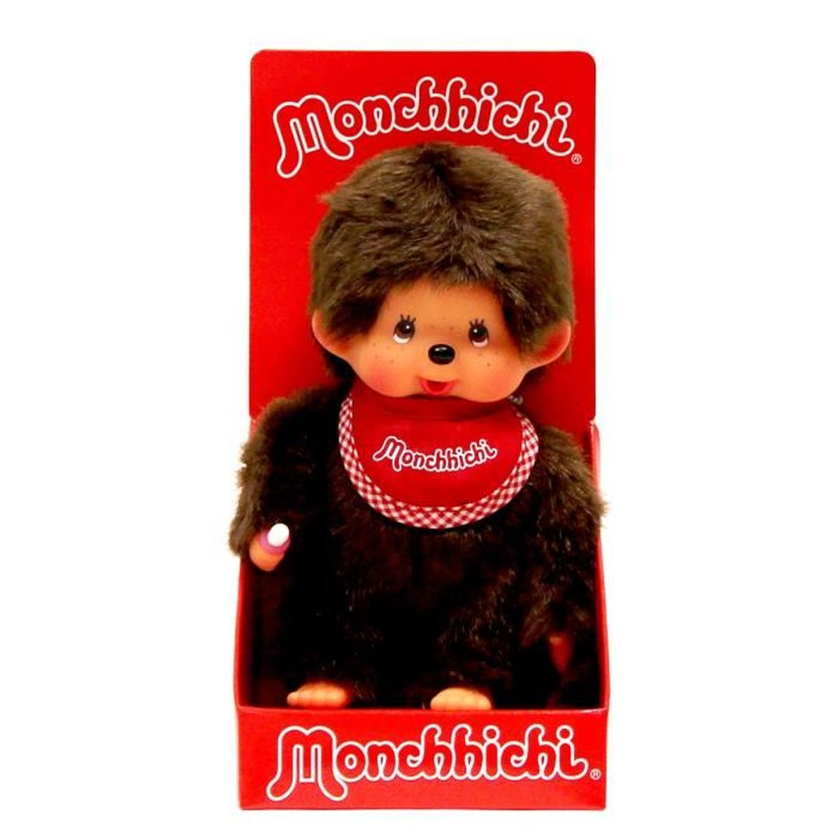 Lalka Monchhichi w czerwonym pudełku. Ma brązowe futro, czerwoną śliniaczek z białym obszyciem i trzyma butelkę. Na pudełku napis 'Monchhichi'.