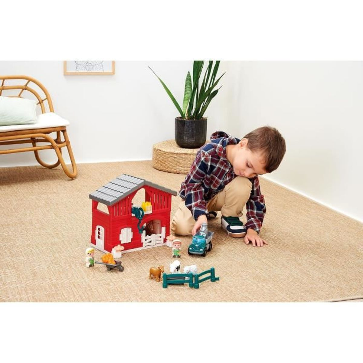 Un bambino gioca con un set di fattoria giocattolo, tra cui un fienile rosso, statuine, un camion e animali, su un tappeto beige.