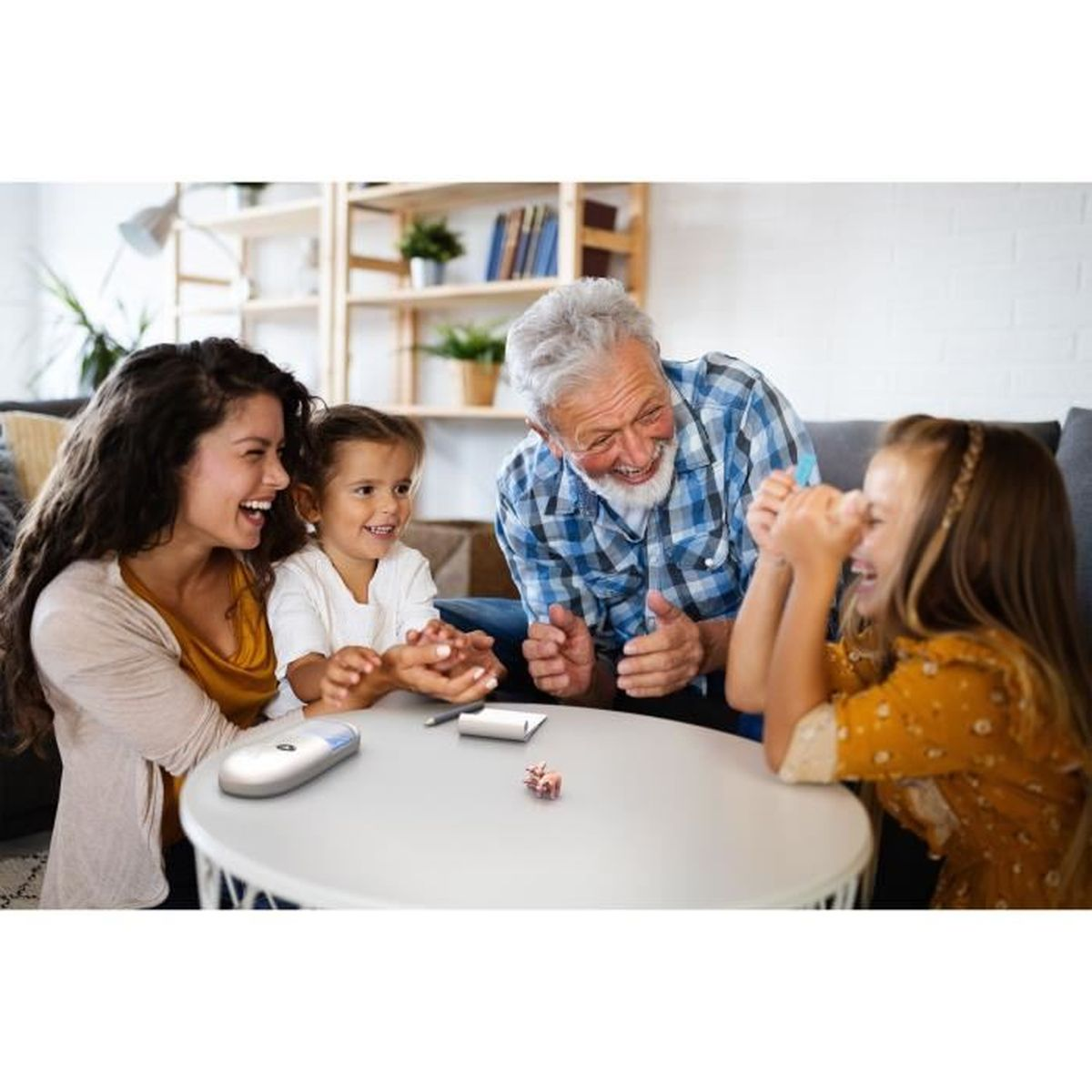 Una famiglia di cinque persone ride intorno a un tavolo. Un gioco e cancelleria sono sul tavolo. Una libreria sullo sfondo.
