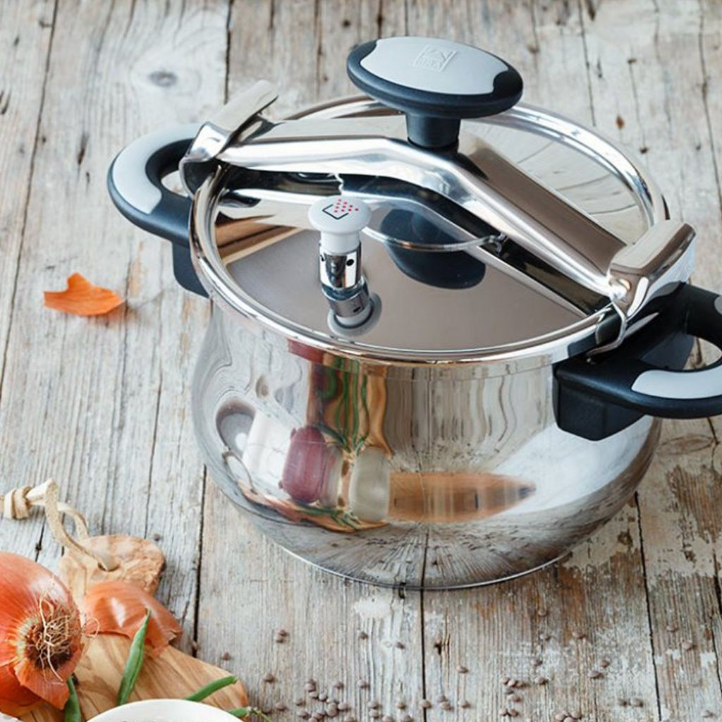 Una olla a presión de acero inoxidable sobre una superficie de madera. Cebollas y verduras en primer plano.