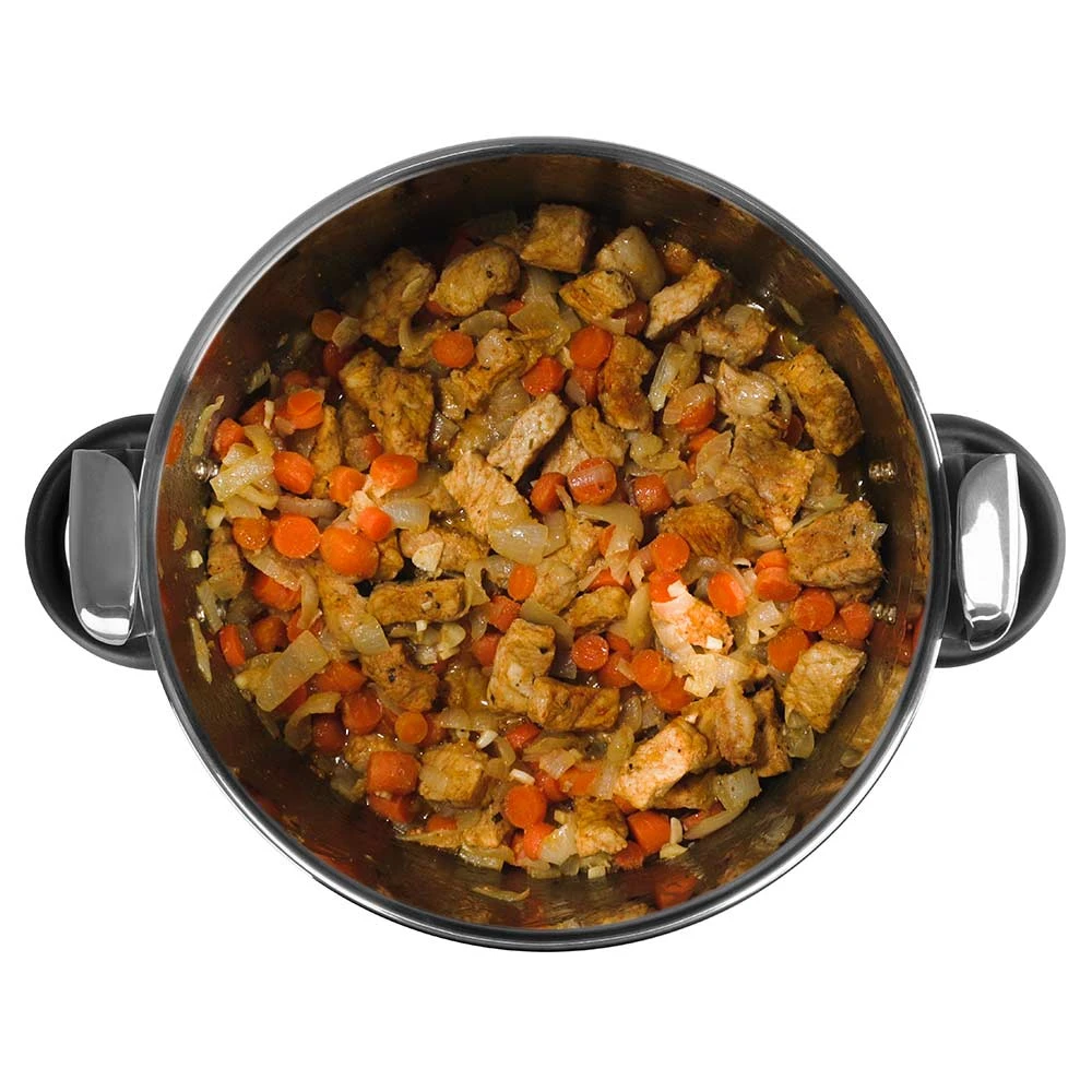 Una olla llena de comida cocinada. Contiene carne en cubos, zanahorias naranjas y cebollas. La olla es de acero inoxidable con asas negras.