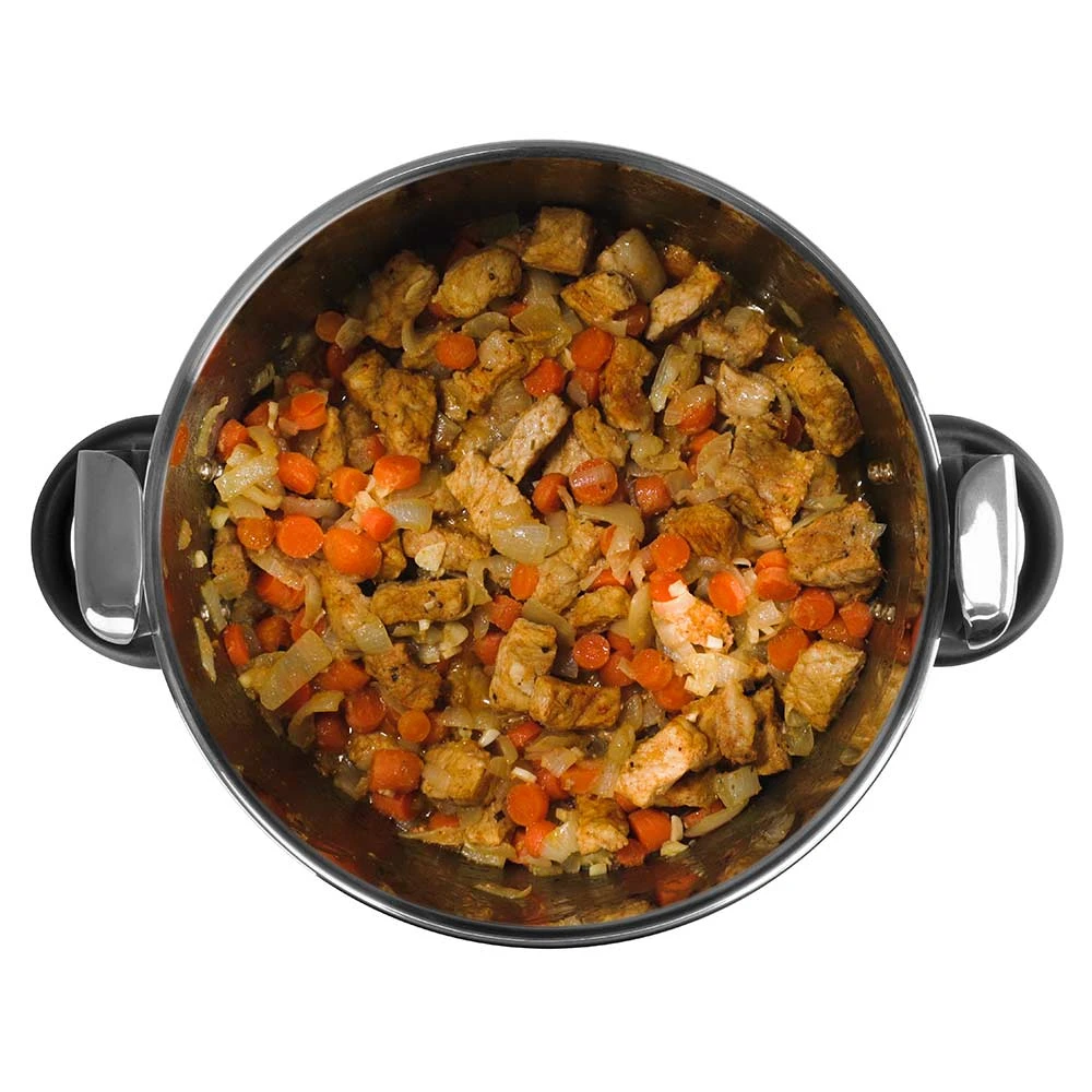 Una olla de acero inoxidable llena de comida cocinada. Contiene trozos de carne, zanahorias naranjas y cebollas, todo mezclado.