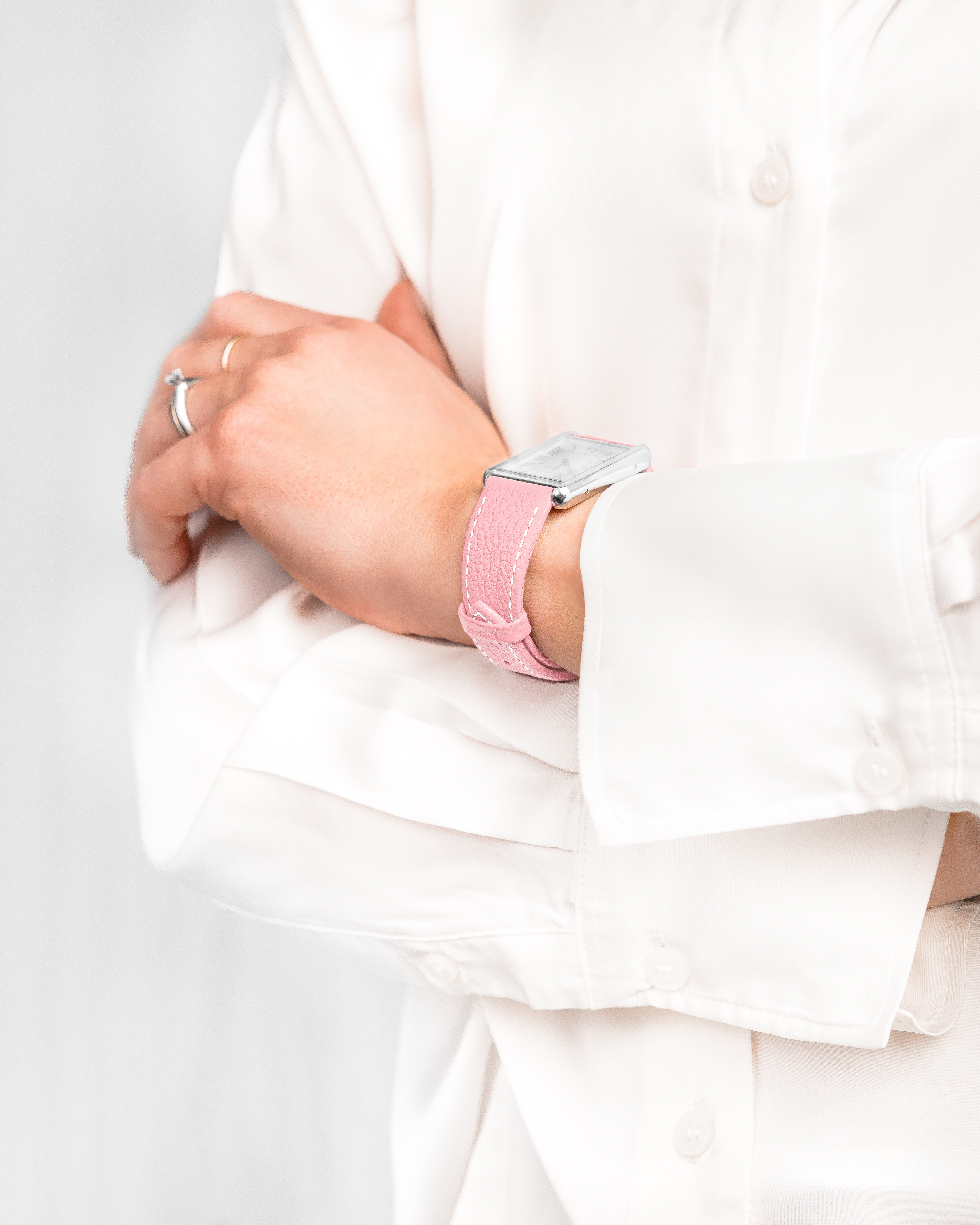 Eine Person in weißem Hemd mit verschränkten Armen. Am Handgelenk befindet sich eine silberne Uhr mit rosa Armband.