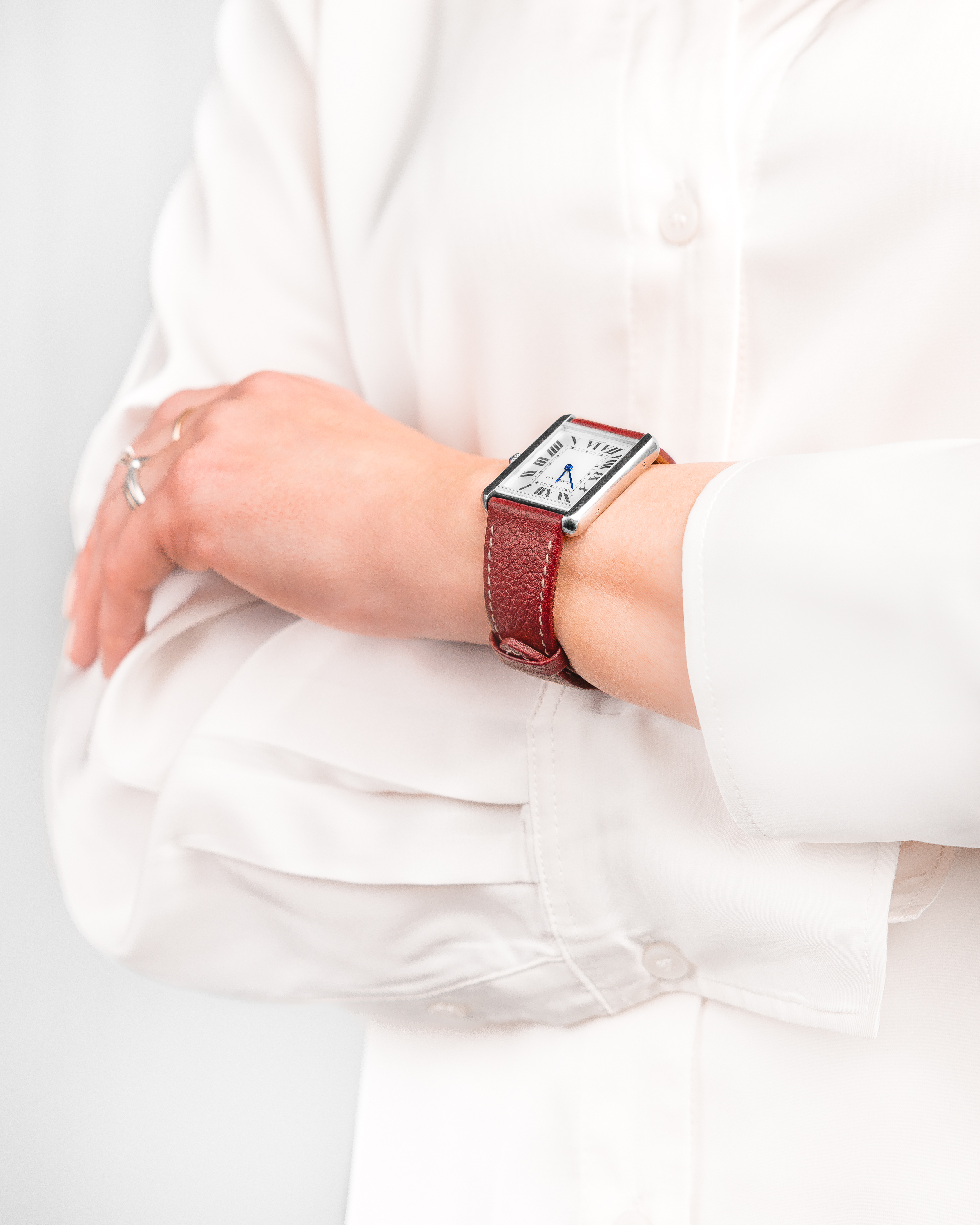 Ein Arm mit einer roten Uhr am Handgelenk. Die Person trägt ein weißes Hemd.