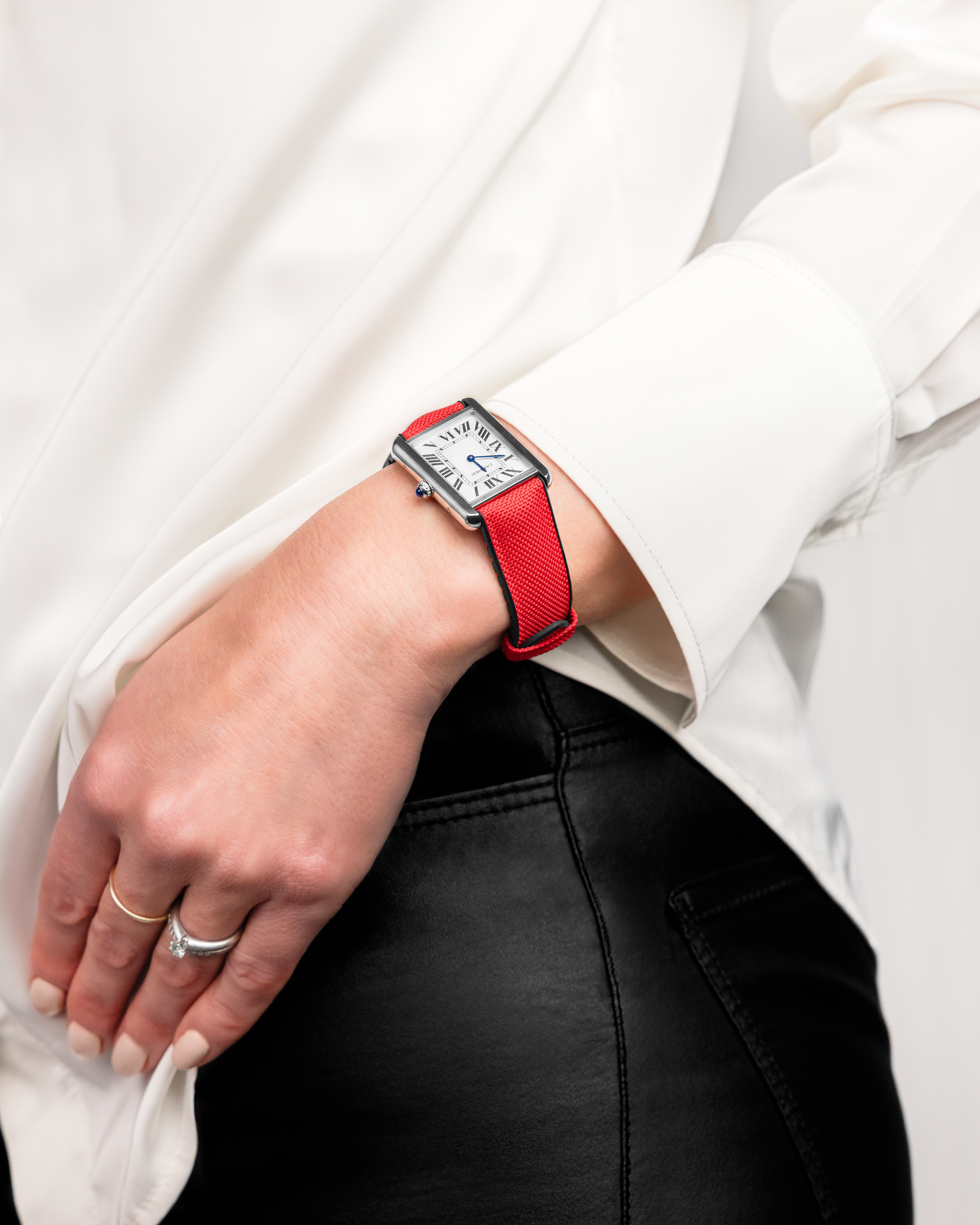 Eine Person trägt eine Uhr mit rotem Armband. Die Person trägt ein weißes Hemd und eine schwarze Hose.