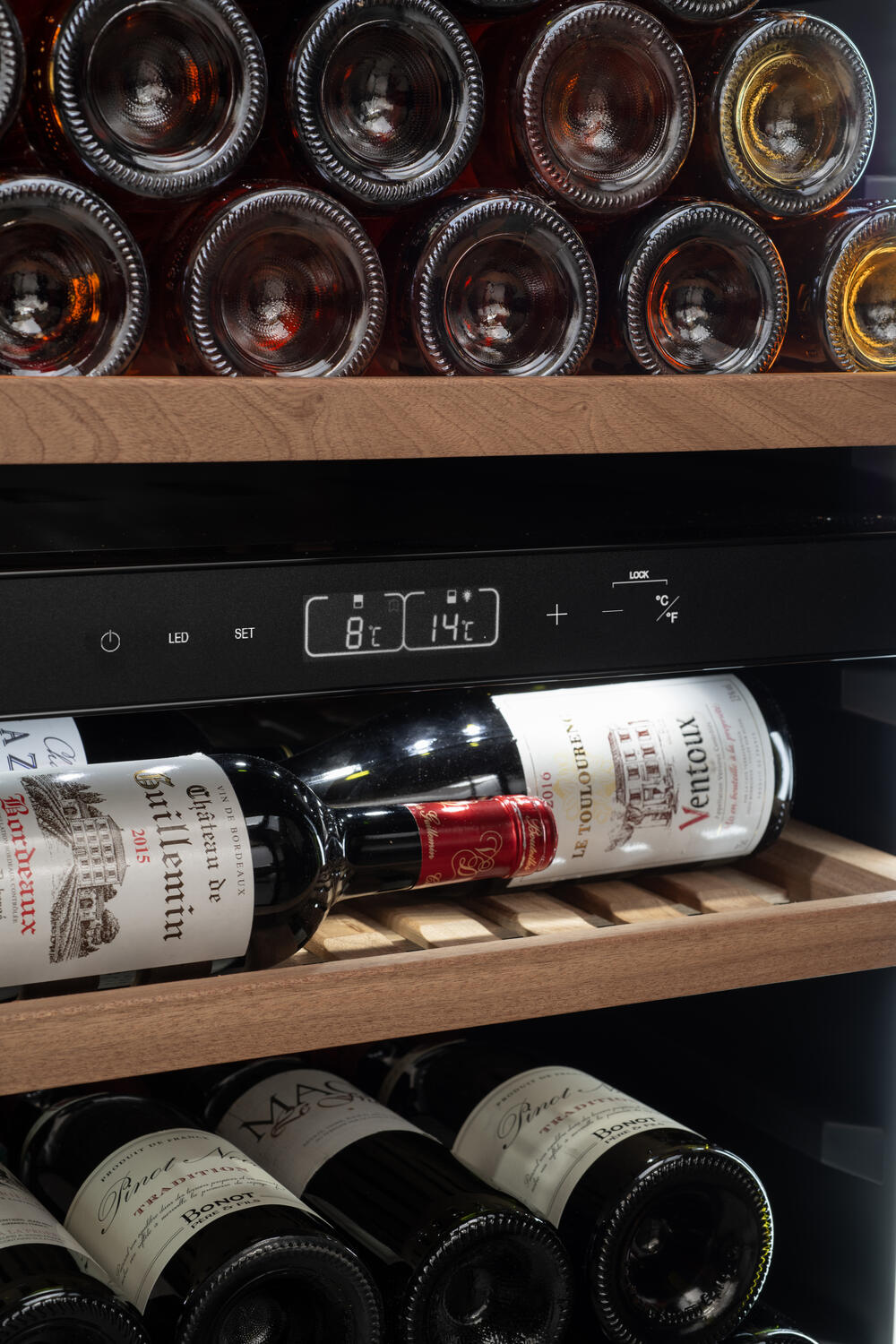 Botellas de vino en un enfriador. Pantalla digital muestra 8°C y 14°C. Estantes de madera con botellas de vino, etiquetas visibles.