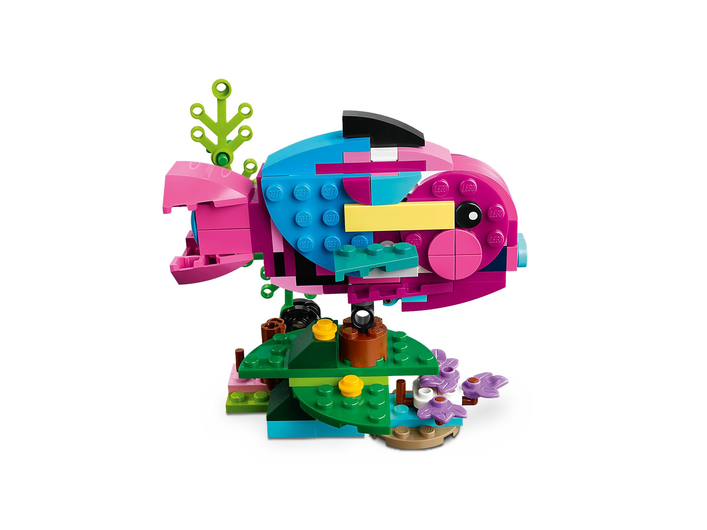 Ein LEGO-Fisch mit rosa, blauen und lila Blöcken, grünem Seegras und lila Blumen auf weißem Hintergrund.