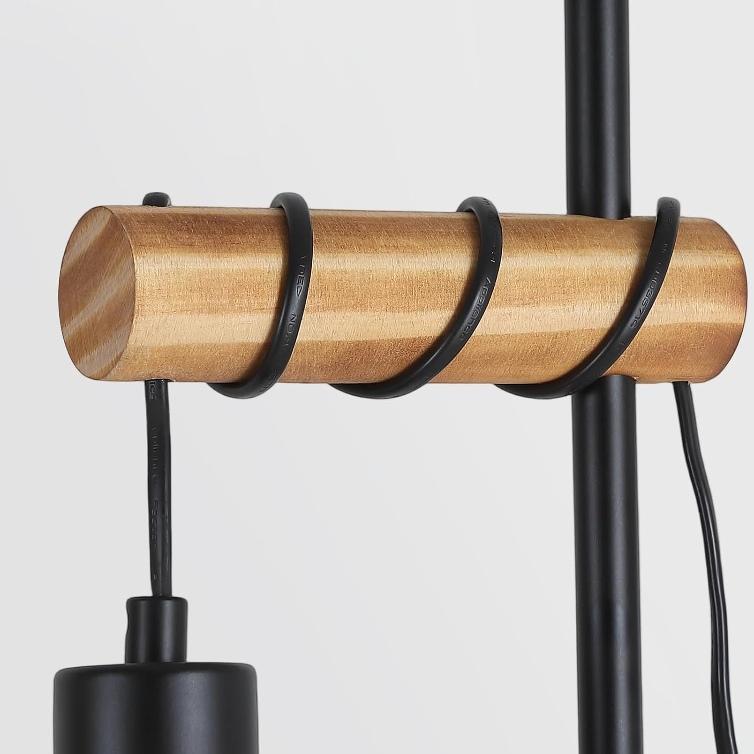 Primo piano di una lampada. Un cilindro di legno è avvolto da fili neri e ha un'asta nera. Lo sfondo è bianco.