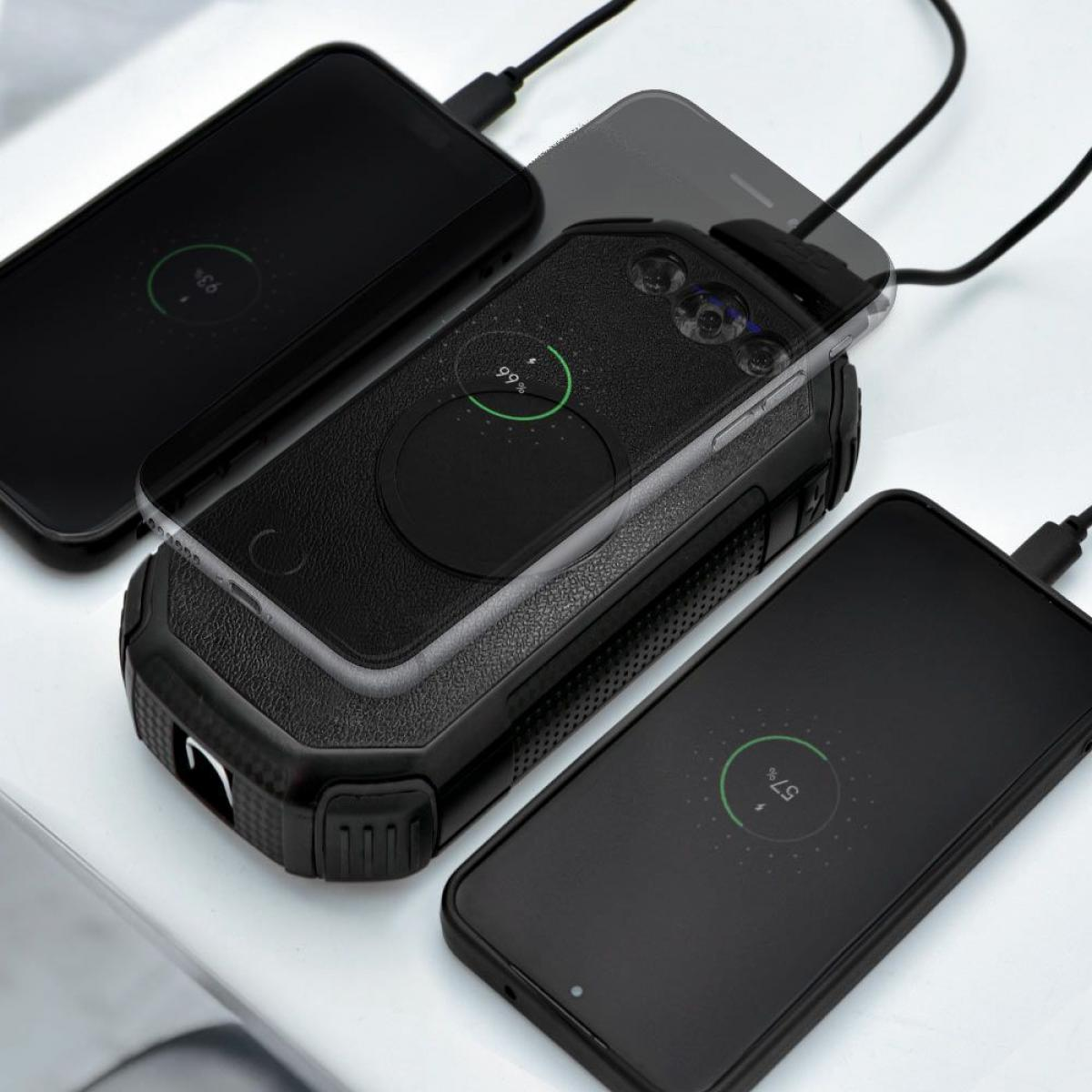 Drie zwarte smartphones die opladen op een wit oppervlak. Elke telefoon toont een oplaadpercentage. Een oplader is zichtbaar.