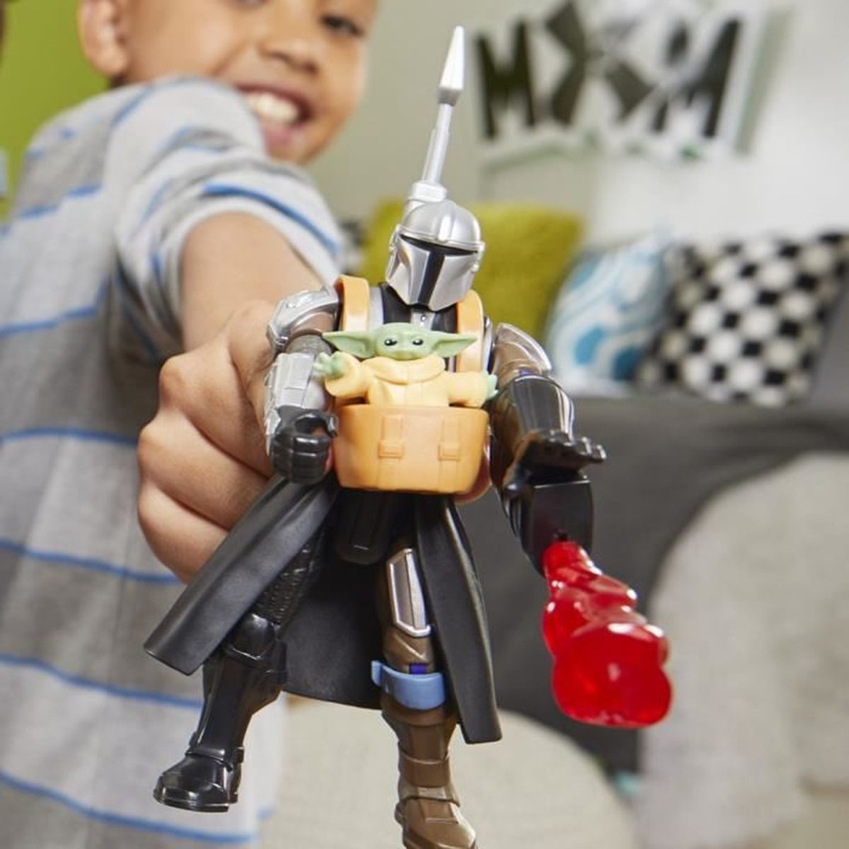 Ein Kind hält eine Mandalorianer-Actionfigur mit Grogu. Das Spielzeug hat einen Umhang und einen roten Schuss. Der Hintergrund ist verschwommen.