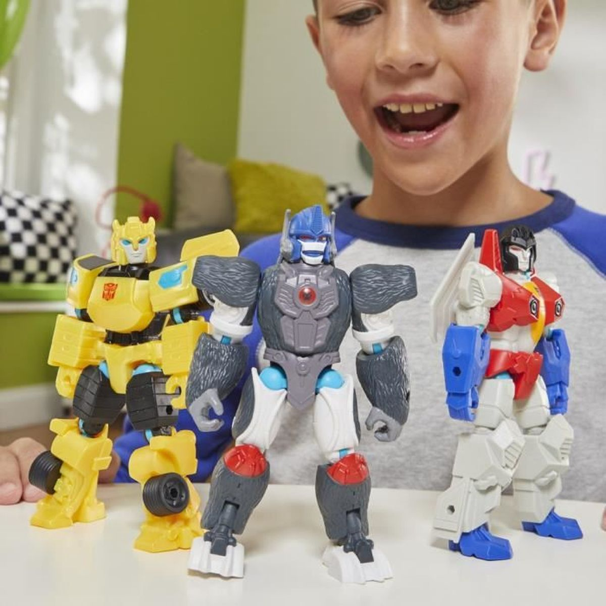 Un niño sonríe a tres juguetes Transformers: uno amarillo, uno gris con forma de gorila y un robot rojo, blanco y azul.