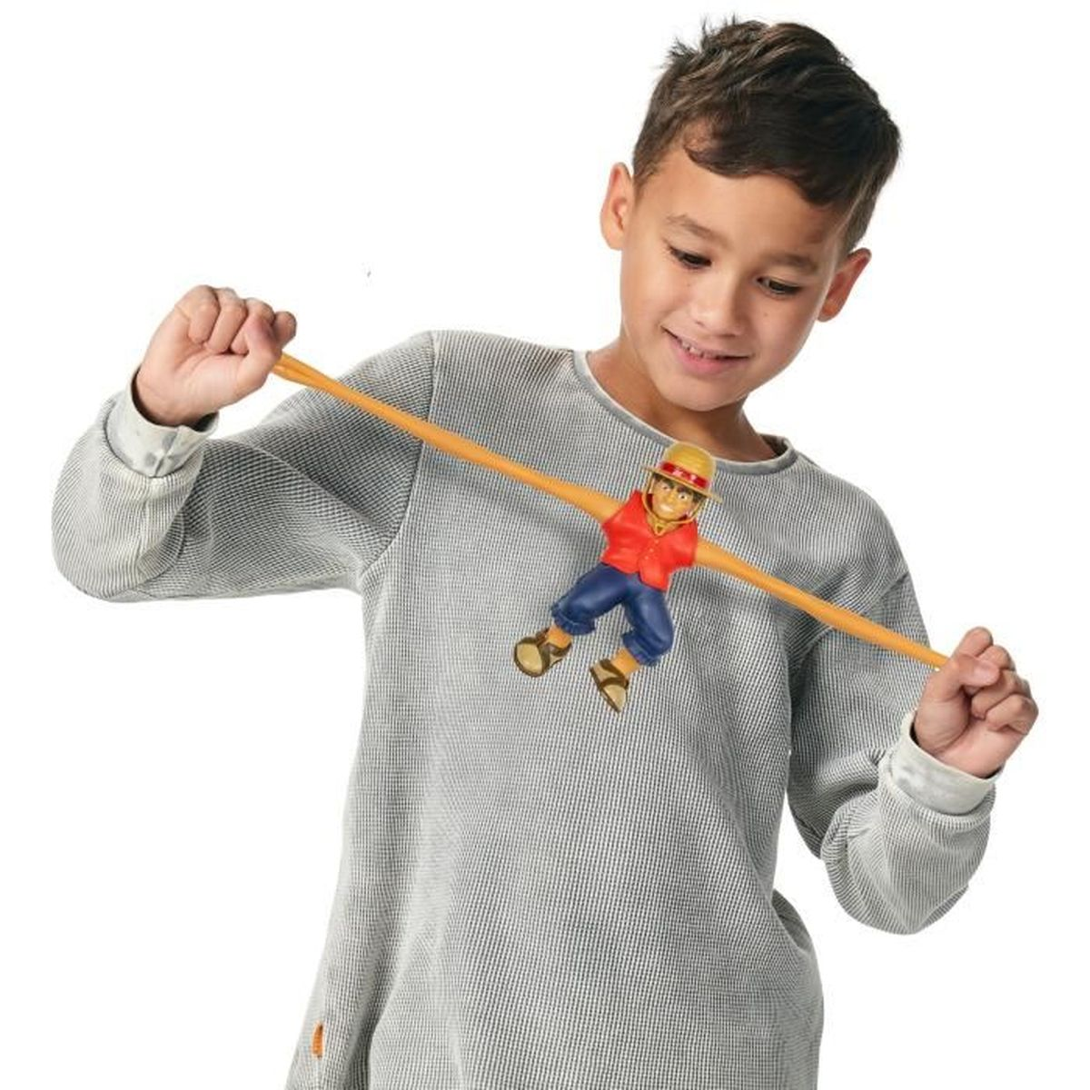 Un niño sonríe mientras sostiene una figura de juguete en un palo de madera. El juguete es un hombre con chaleco rojo, pantalón azul y sombrero.